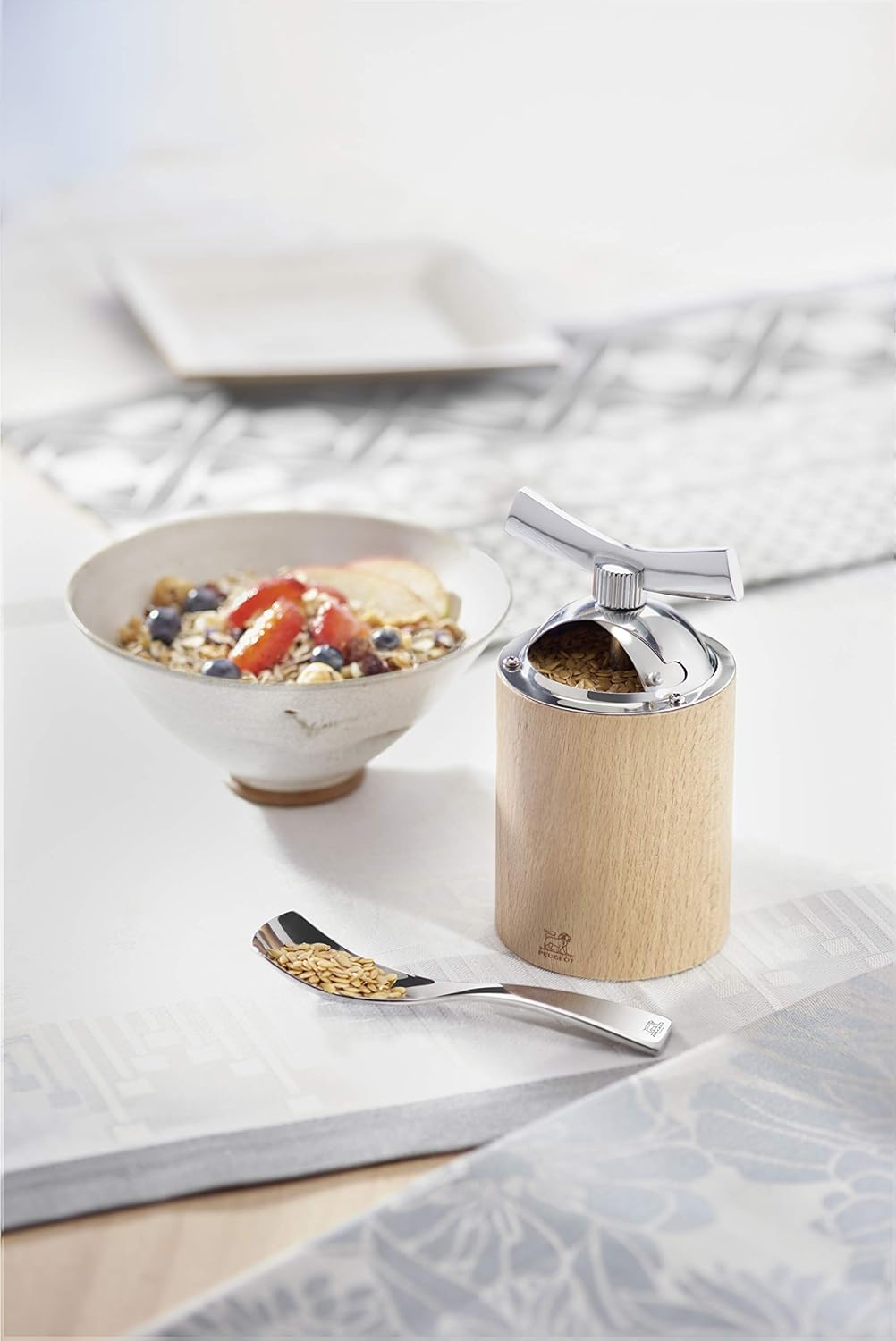Peugeot Isen Manual Flax Seed Mill on a table next to a bowl of cereal
