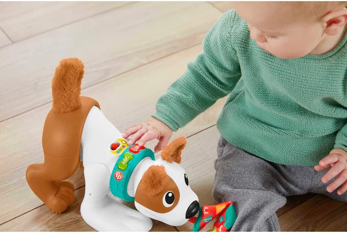 A baby sitting on a wooden floor, pressing the light-up buttons on the collar of the Fisher-Price Crawl-With-Me Puppy Bello.