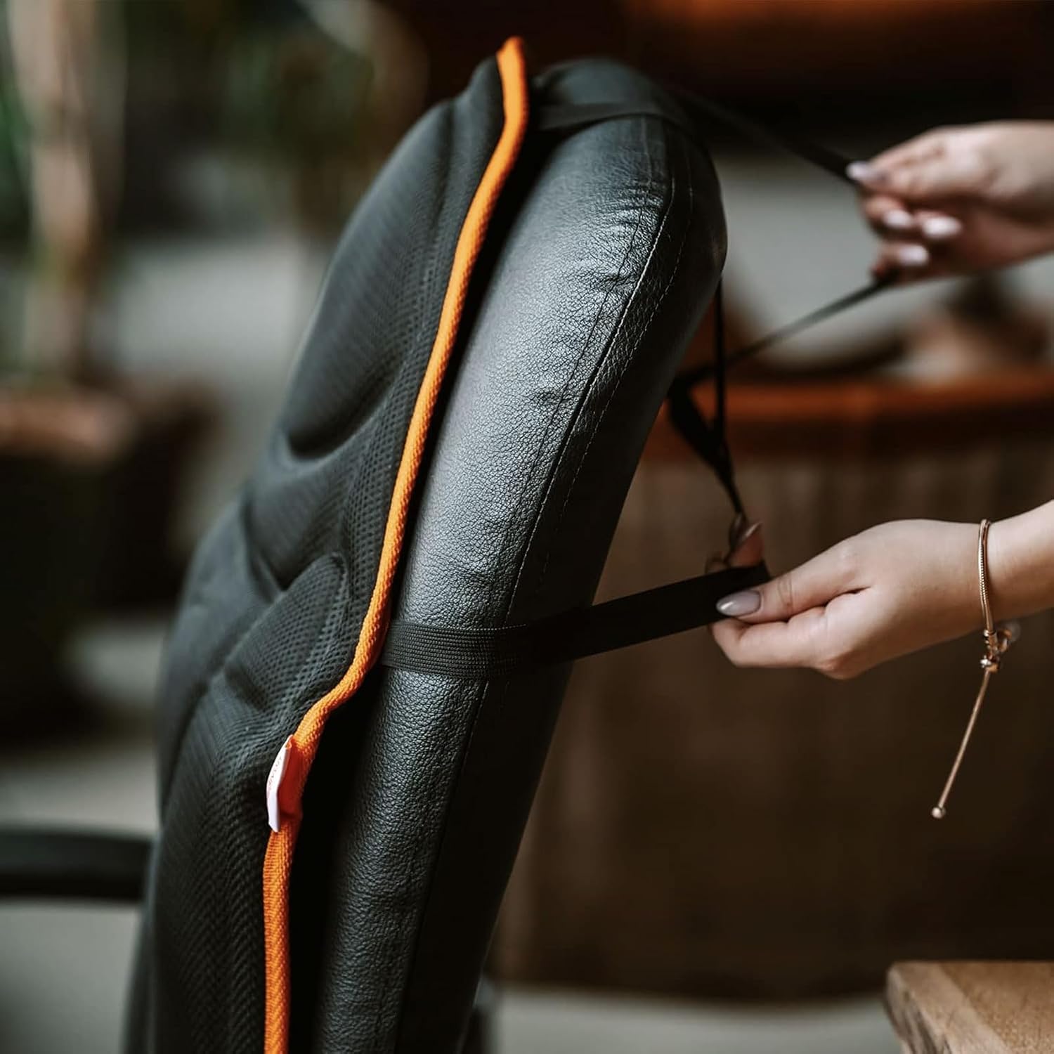 Hands adjusting elastic straps on the back of the Medivon Cosy Mesh Massage Mat to secure it to a chair.