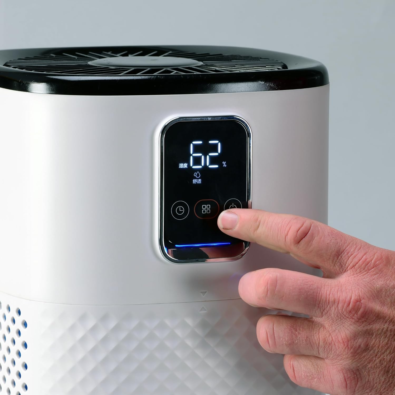 A finger pressing the power button on the digital control panel of the EdenPURE Mist-Free Humidifier.