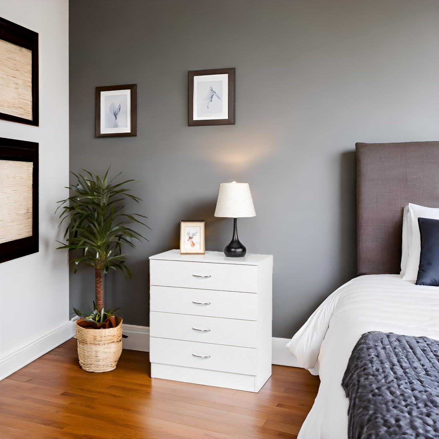 The white dresser placed in a modern bedroom setting next to a bed, with a plant and lamp, showing its integration into a living space.