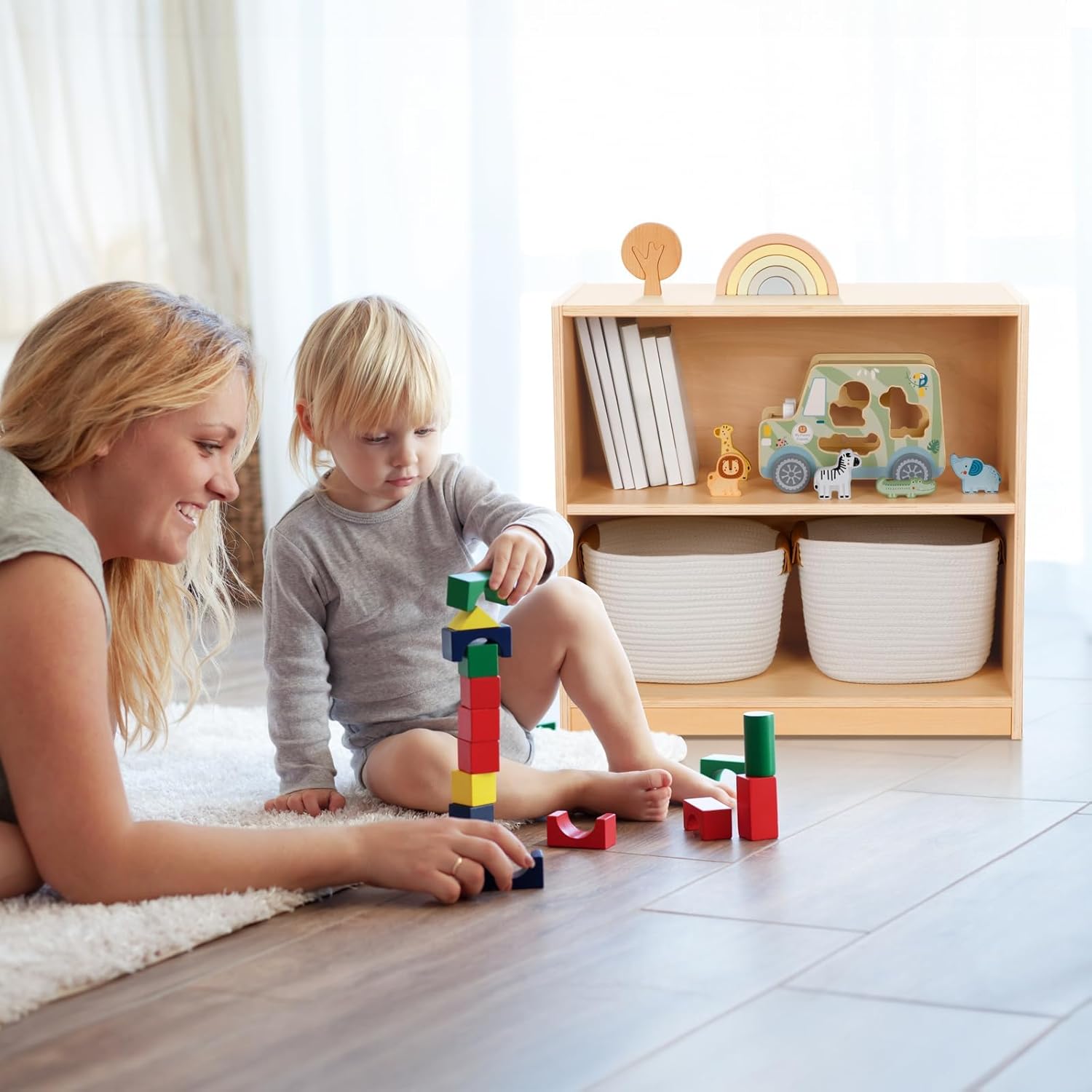 A child playing with blocks on the floor next to the OOOK Montessori Bookshelf, which is filled with books and toys.