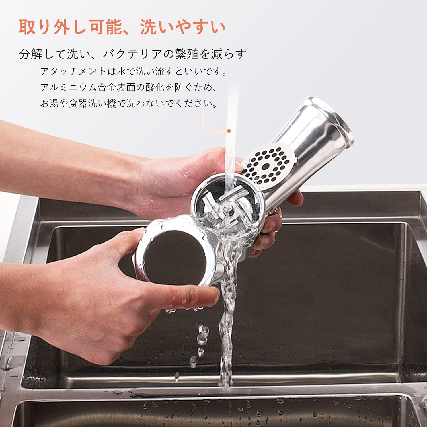 Hands washing the disassembled meat grinder head under running water in a sink.