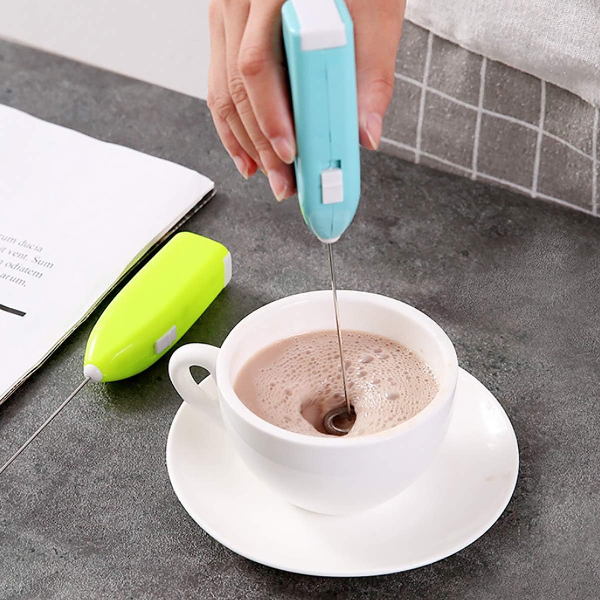 A light blue UpTuoLi milk frother actively frothing coffee in a white cup, with a green frother in the background.