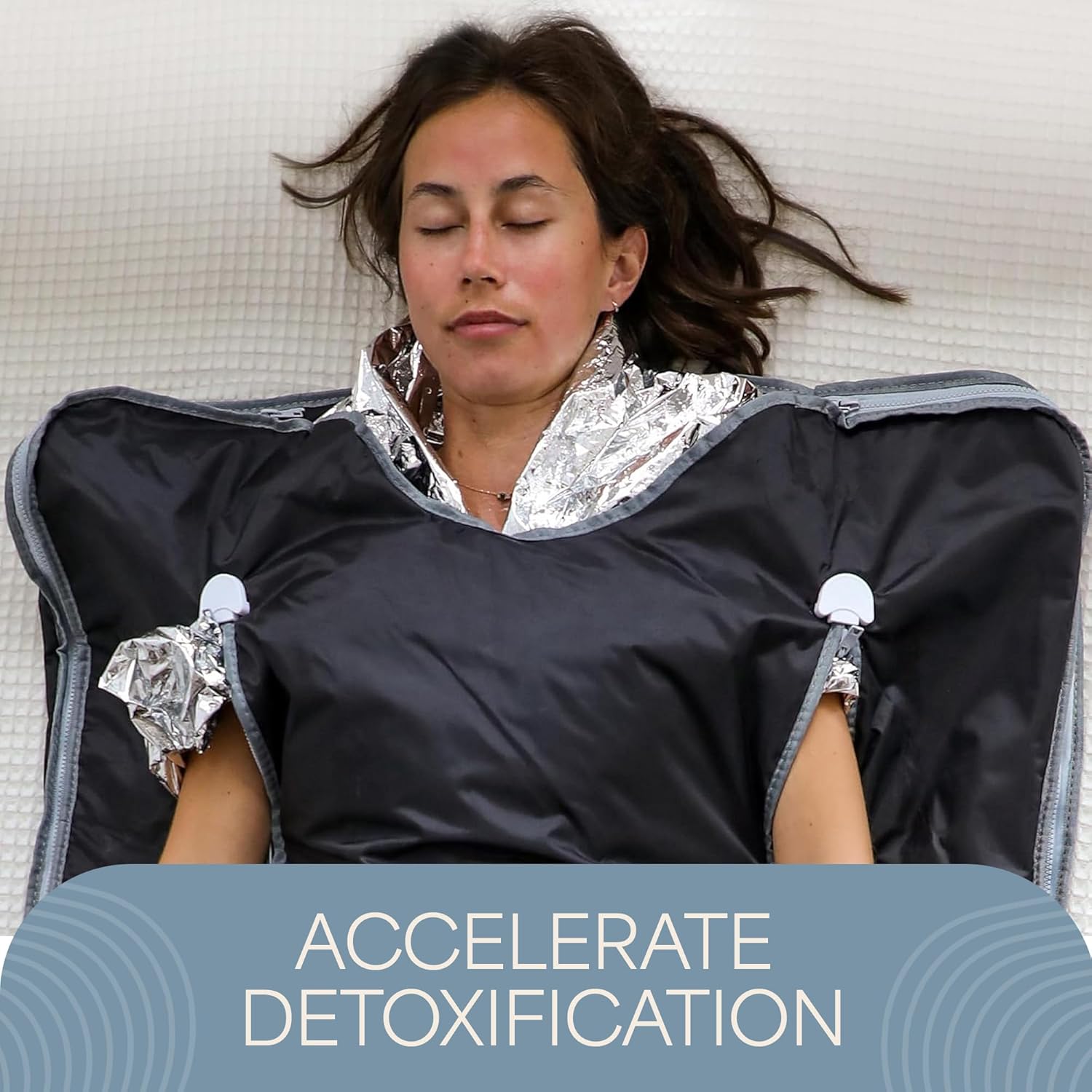Woman lying relaxed in a sauna blanket with a foil wrap, text overlay 'ACCELERATE DETOXIFICATION'.