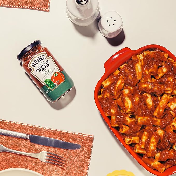 Mesa posta com um pote de molho de tomate rústico Heinz basílico ao lado de uma travessa de macarrão com molho, talheres e porta-guardanapos
