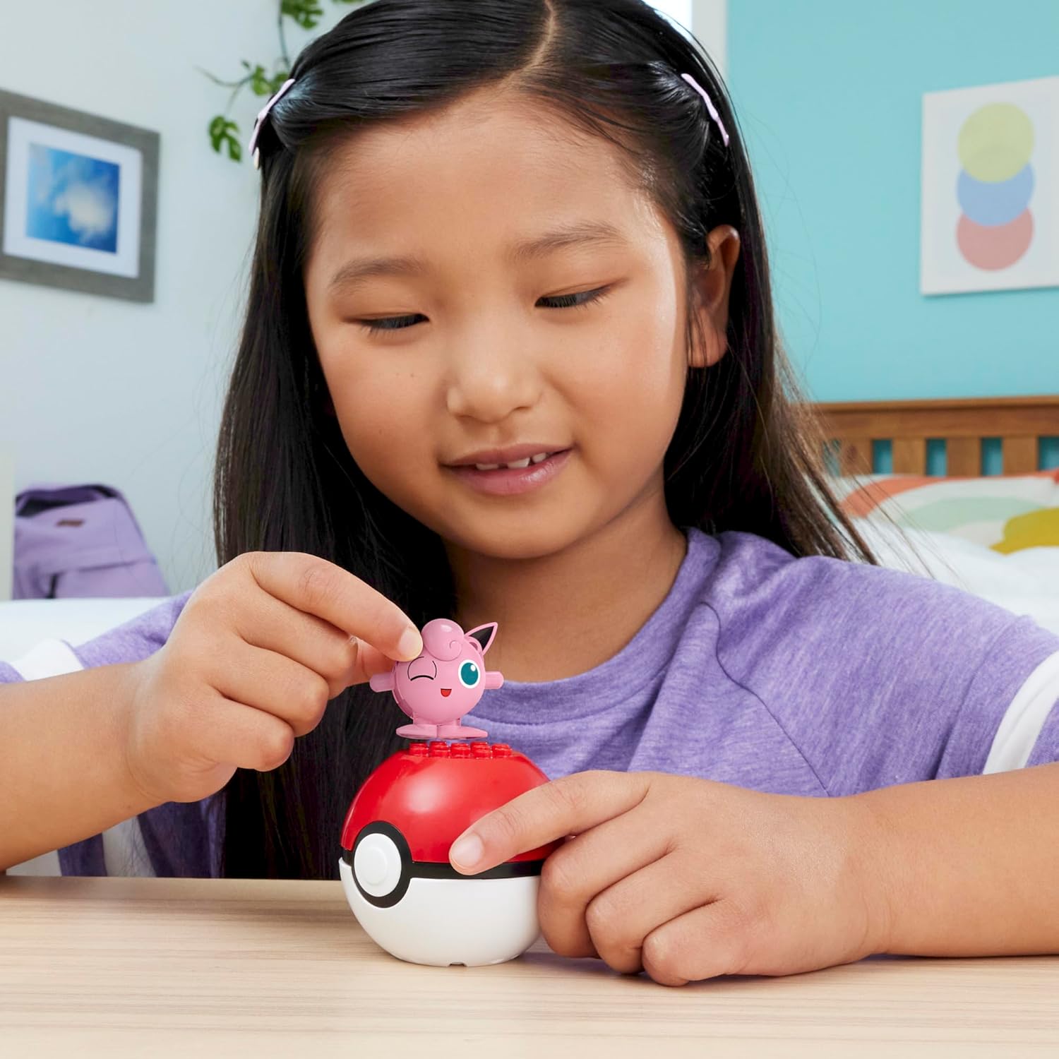 A child placing the assembled Jigglypuff figure onto the top of the Poké Ball construction toy.