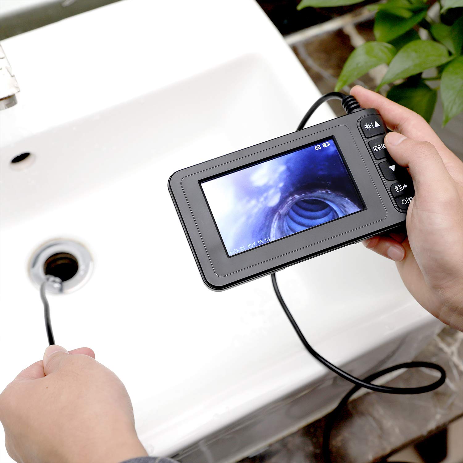 Eine Person hält das Endoskop und führt die Kamerasonde in einen Abfluss ein, wobei der Bildschirm das Innere zeigt. view des Rohres.