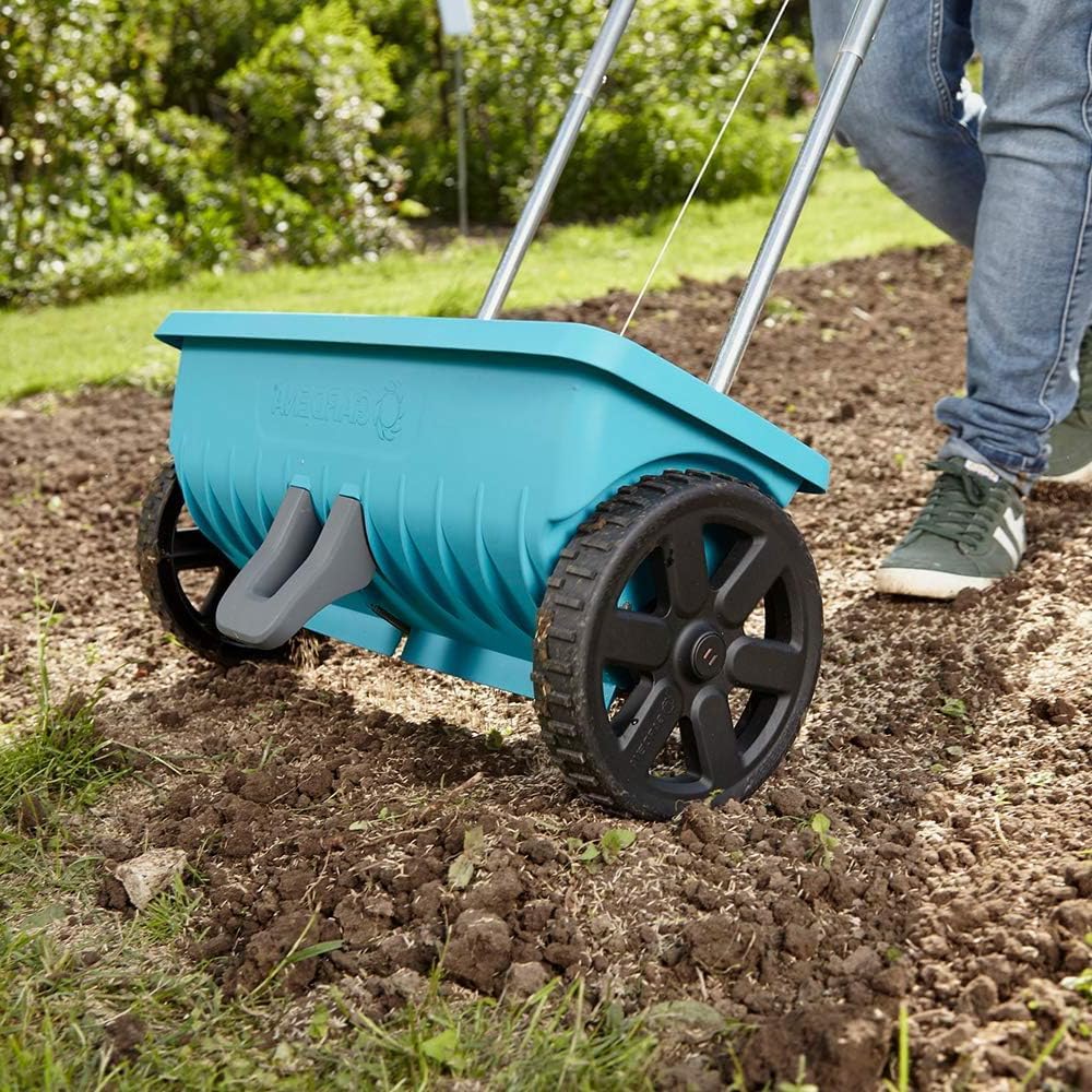 Gardena Spreader L being pushed across tilled garden soil.