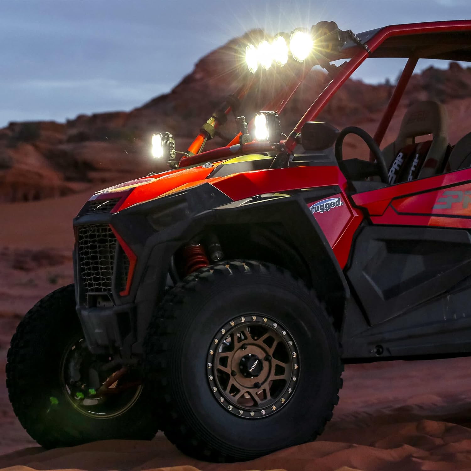 Red UTV/side-by-side vehicle with KC Hilites Flex ERA 4 LED light pods mounted on the A-pillars and roof, parked in a desert landscape at dusk.