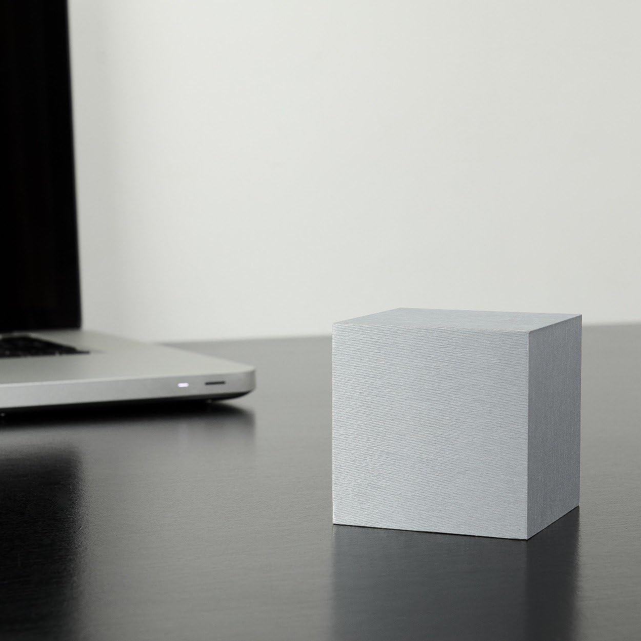 Gingko Design Cube Alarm Clock with its display off, sitting on a dark desk next to a laptop.