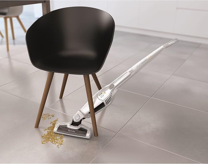 Aspirador de pó vertical Electrolux Ergorapido sendo utilizado para limpar sujeira perto de uma cadeira preta