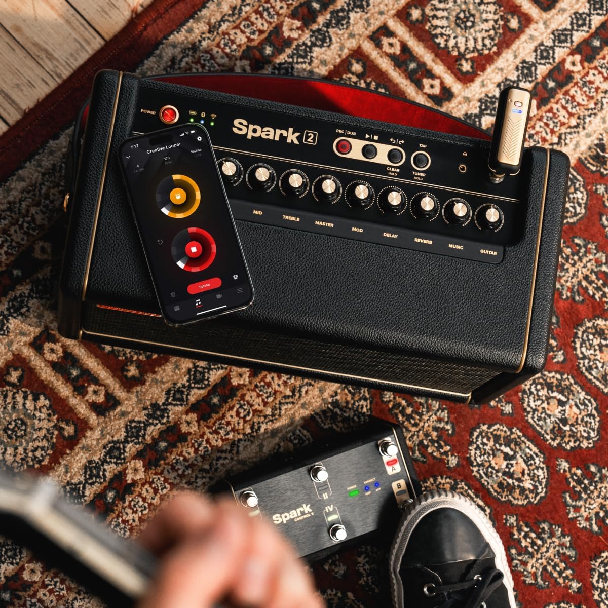 Overhead view of the Positive Grid Spark 2 amplifier with a smartphone displaying the Spark app's interface for tone customization.