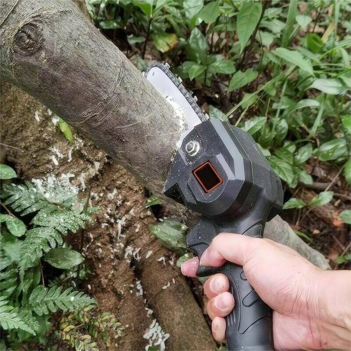 A person's hand holding a mini chainsaw actively cutting a tree branch.