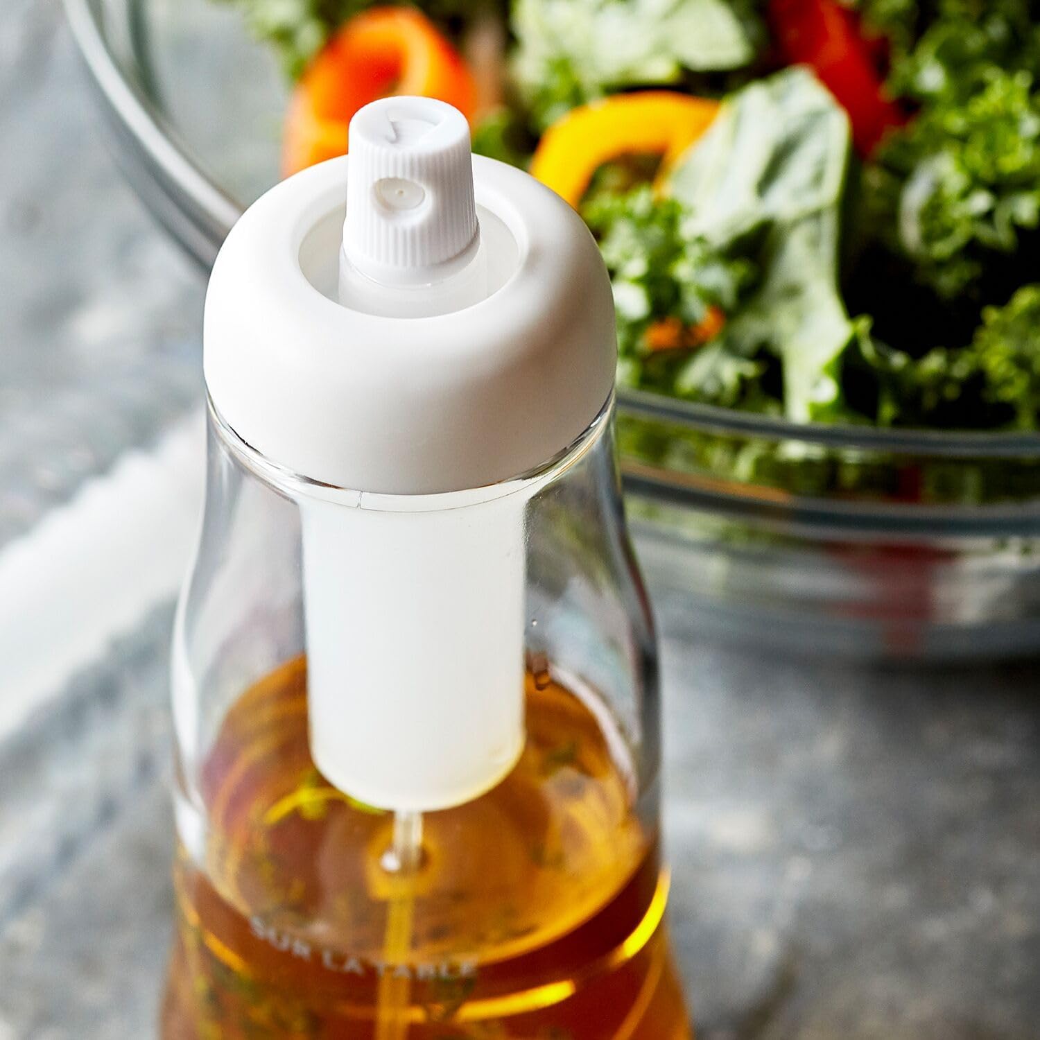 Close-up of the Sur La Table Pump Action Oil Mister's top, showing the pump mechanism and the clear bottle filled with oil.
