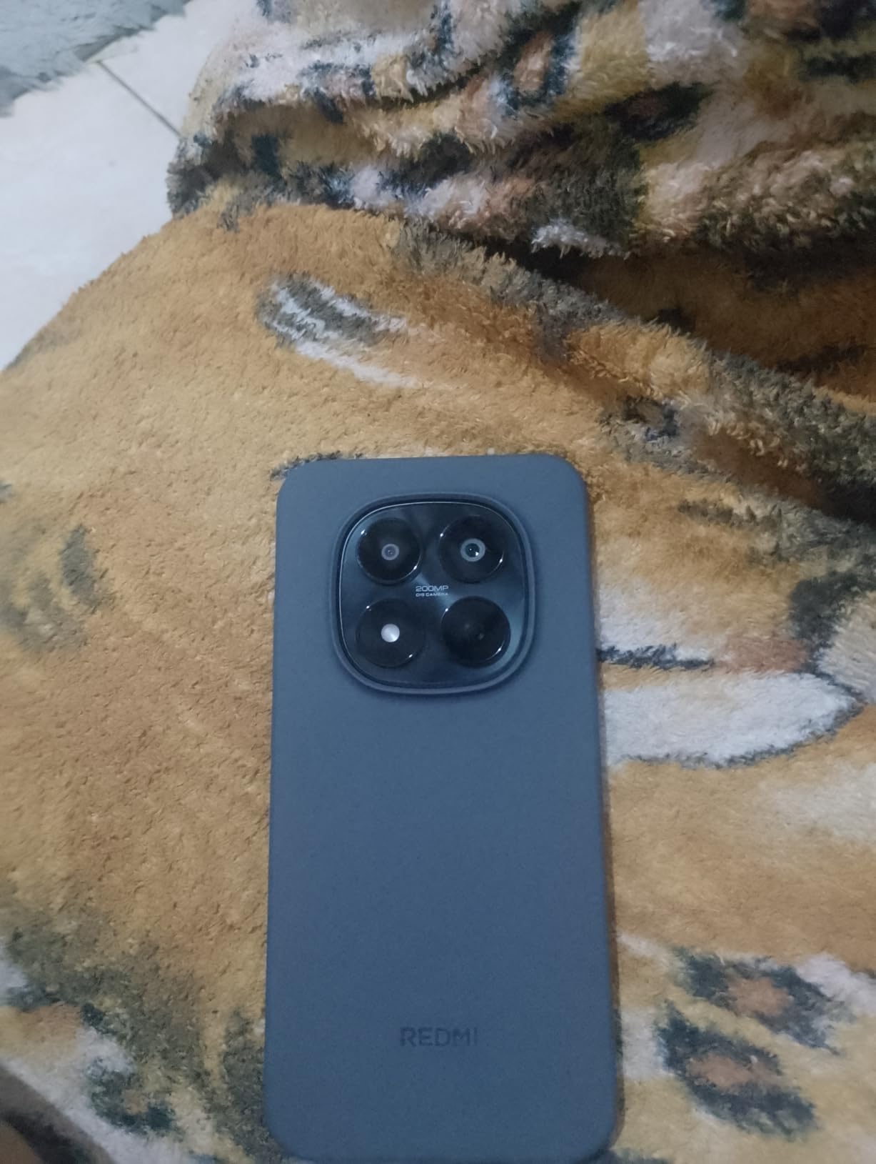 Smartphone cinza com a câmera quádrupla visível em uma coberta felpuda.