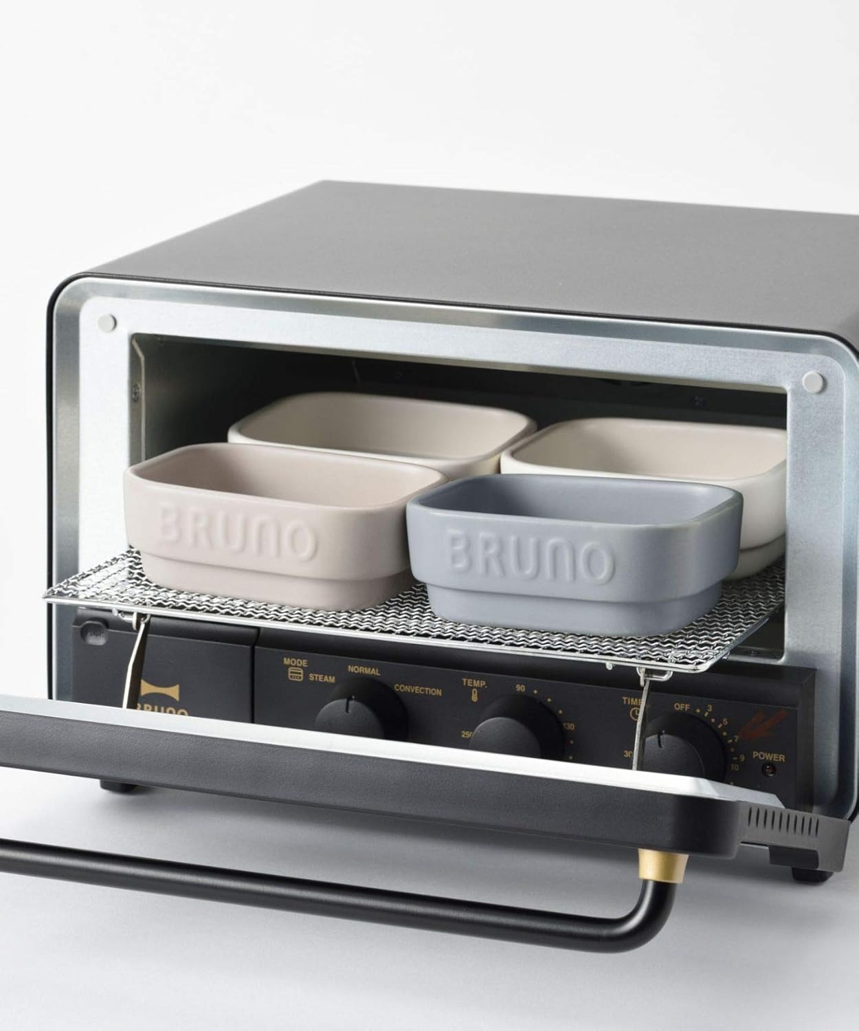 Four BRUNO ceramic toaster cookers arranged on the rack inside a toaster oven, demonstrating maximum capacity.