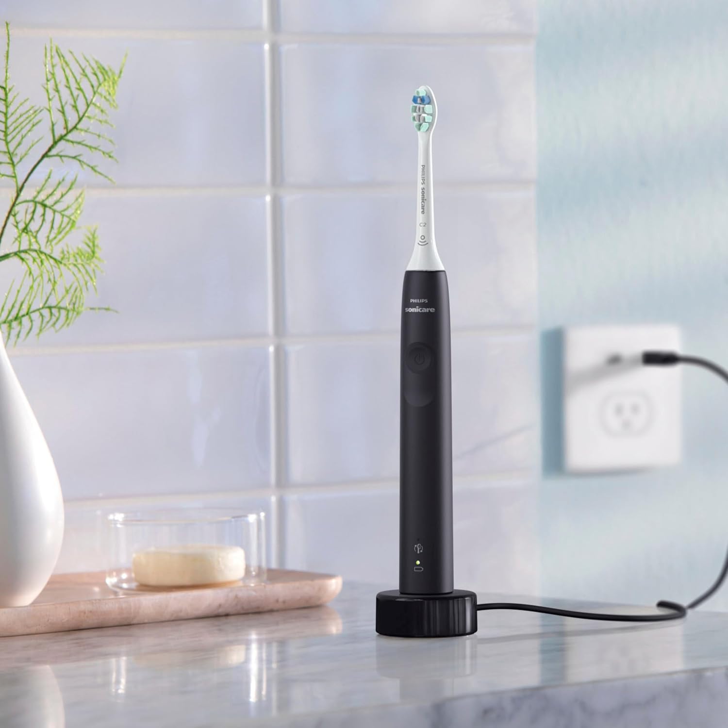 A black Philips Sonicare electric toothbrush handle placed on its charging base, plugged into a wall outlet.