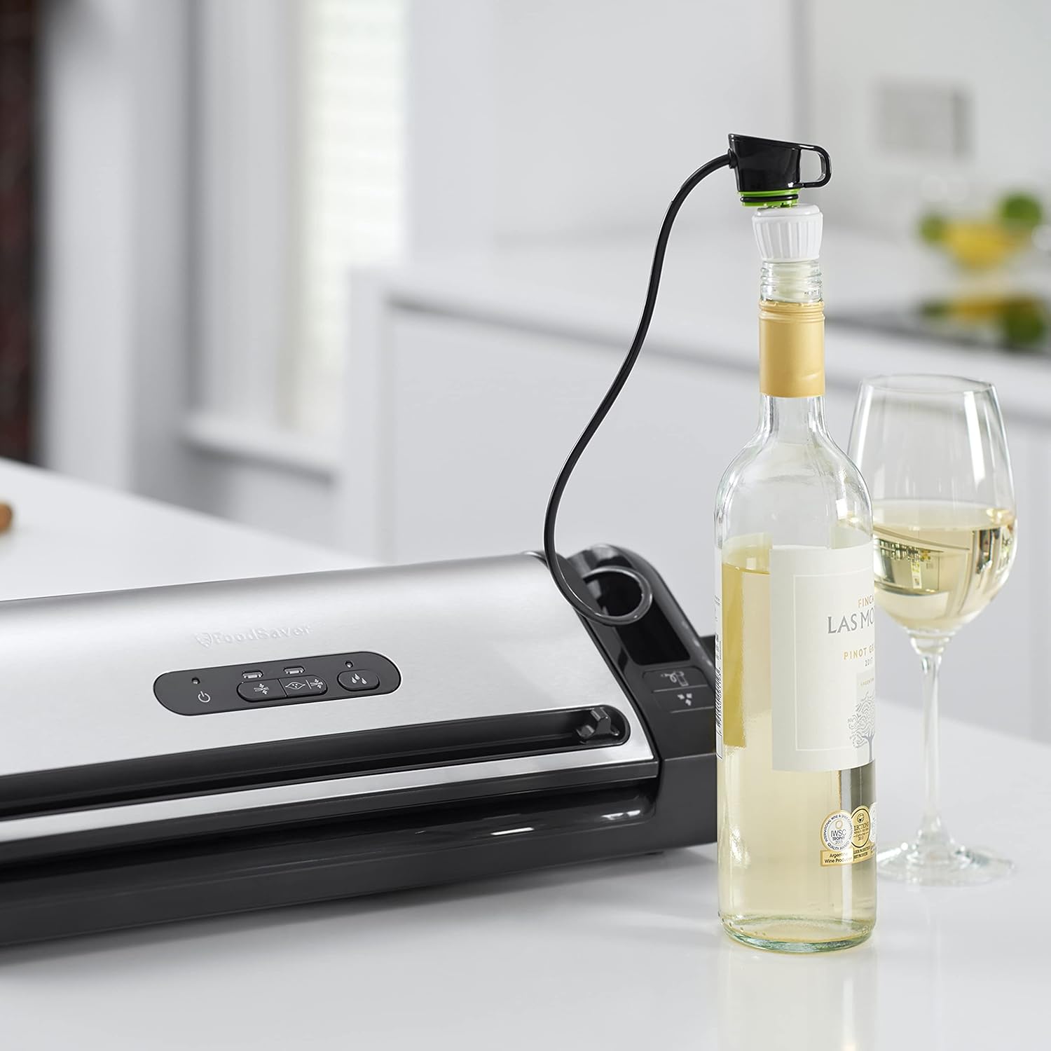 A FoodSaver FFS017X vacuum sealer with its handheld accessory connected to a wine stopper, preserving an open bottle of white wine.