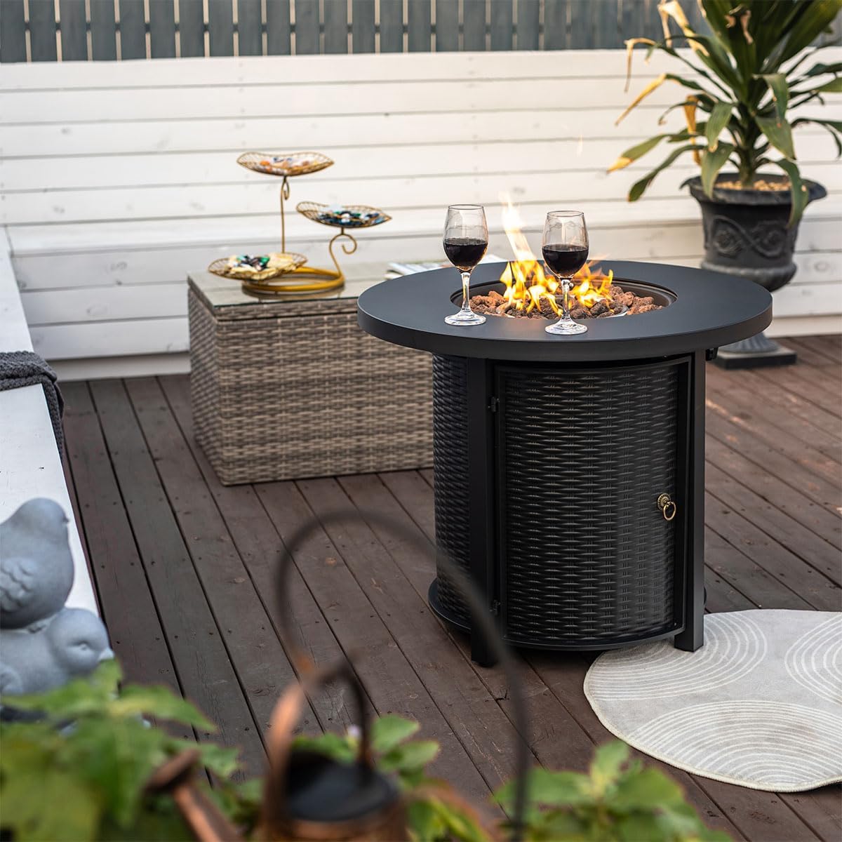 AJ ENJOY 30-inch Round Propane Fire Pit Table on a patio with a wicker side table