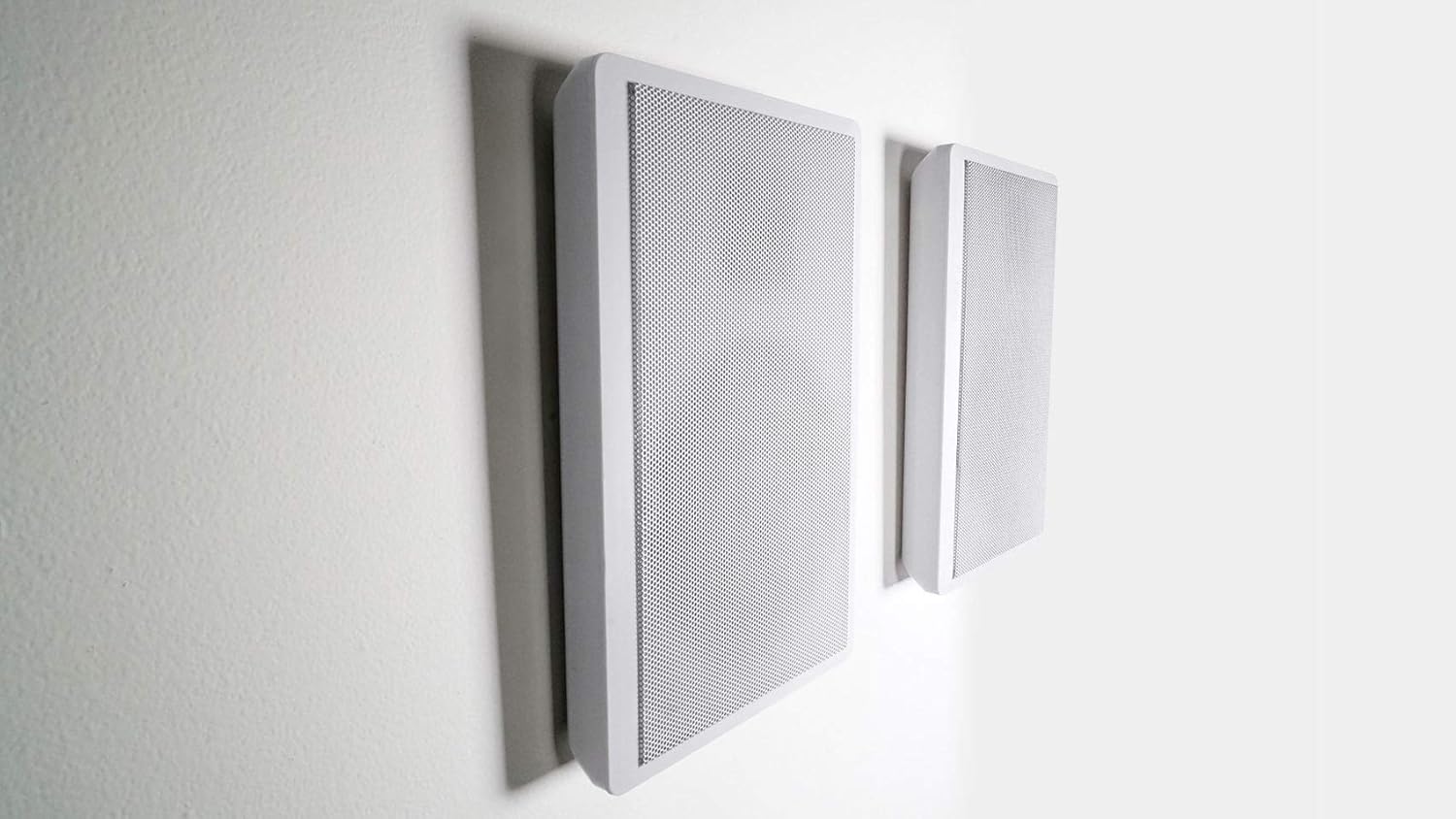 Two white slim speakers mounted on a white wall