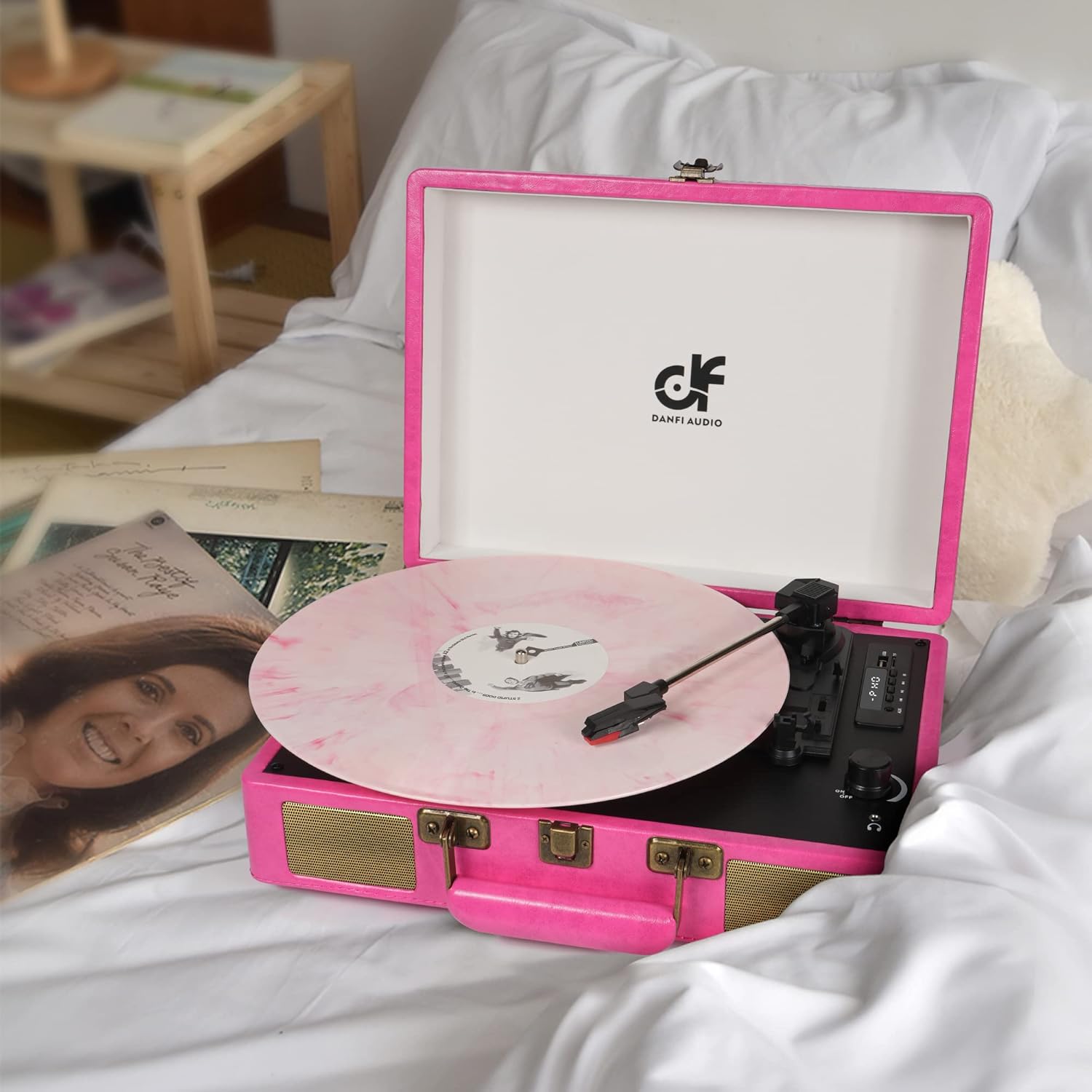 A pink suitcase record player with a pink vinyl record playing on a white surface.