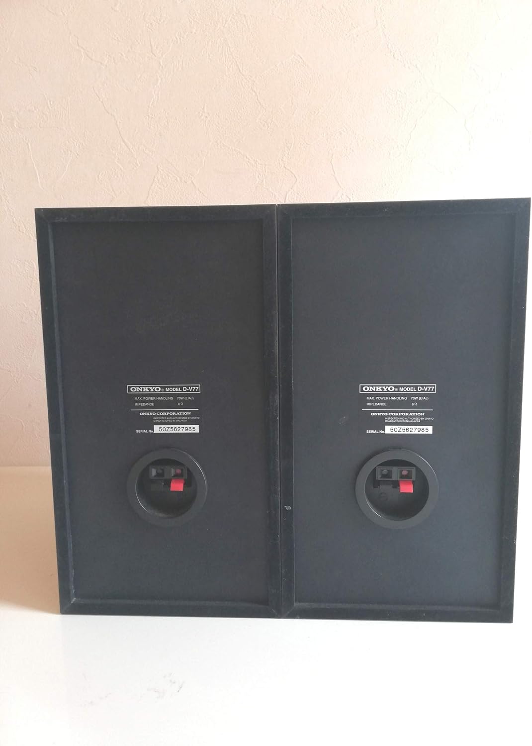 Rear view of the ONKYO D-V77 speakers showing speaker terminals and model information.