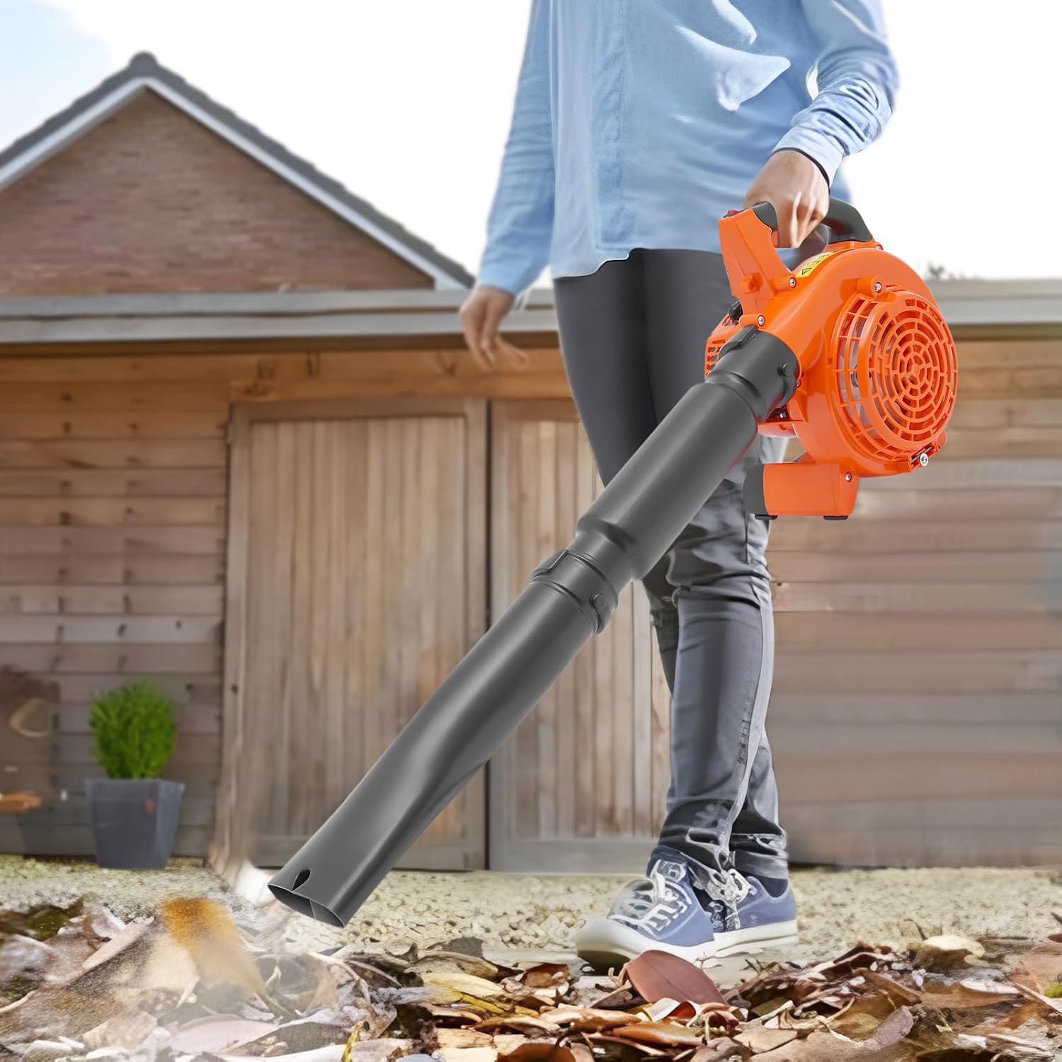 A person operating the CNCEST 26CC Gas Leaf Blower outdoors, clearing leaves from a paved area near a shed.