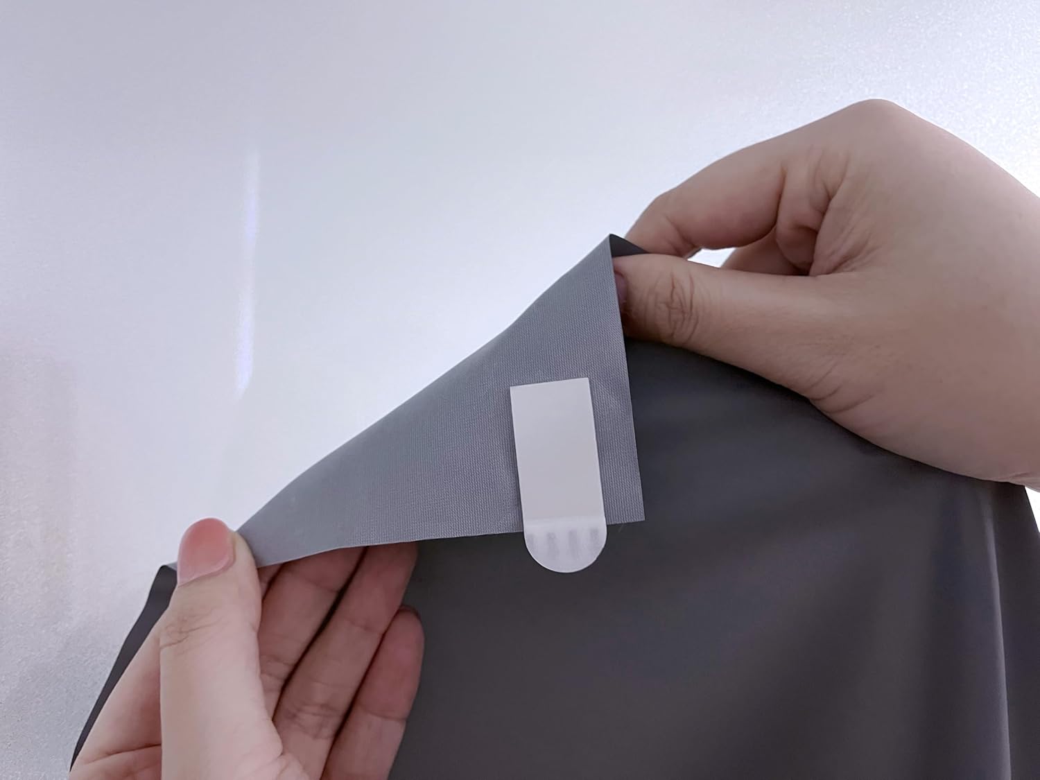 Hands applying a white adhesive strip to the corner of the projector screen.