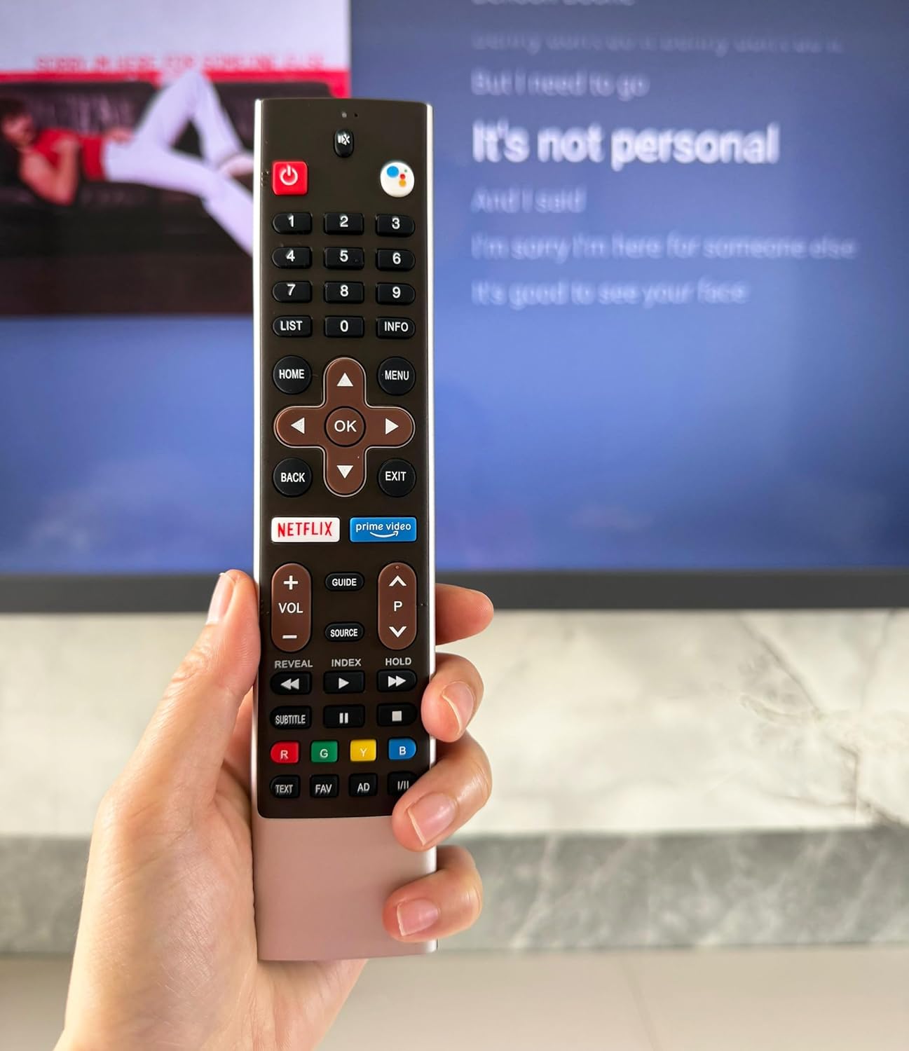Hand holding the LOMCA remote control in front of a Skyworth TV