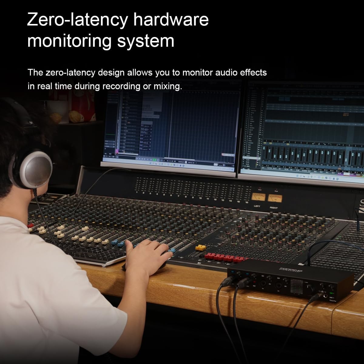 A person operating a large audio mixer console with the TOPPING E4X4 Pre USB Audio Interface connected, demonstrating real-time monitoring during a recording or mixing session.