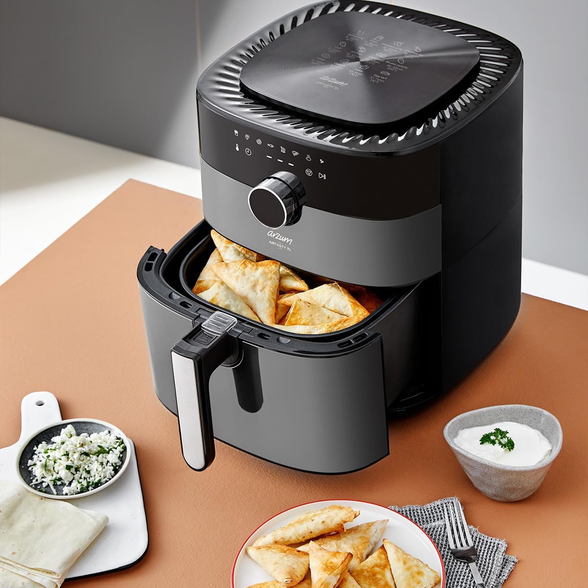 Air fryer with a basket of golden-brown pastries, served with a dip