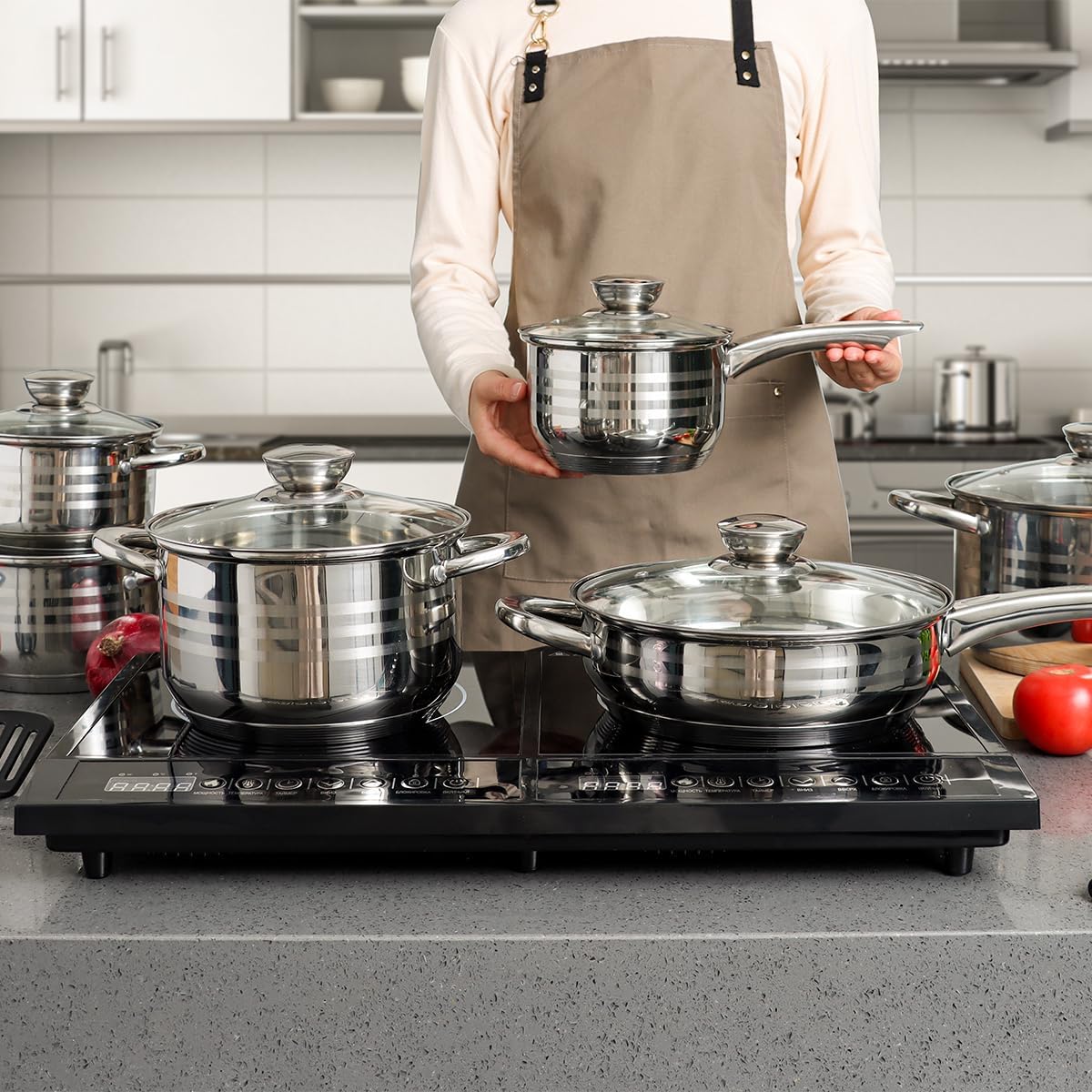 A person holding a small pot from the set, with other pots on an induction hob.