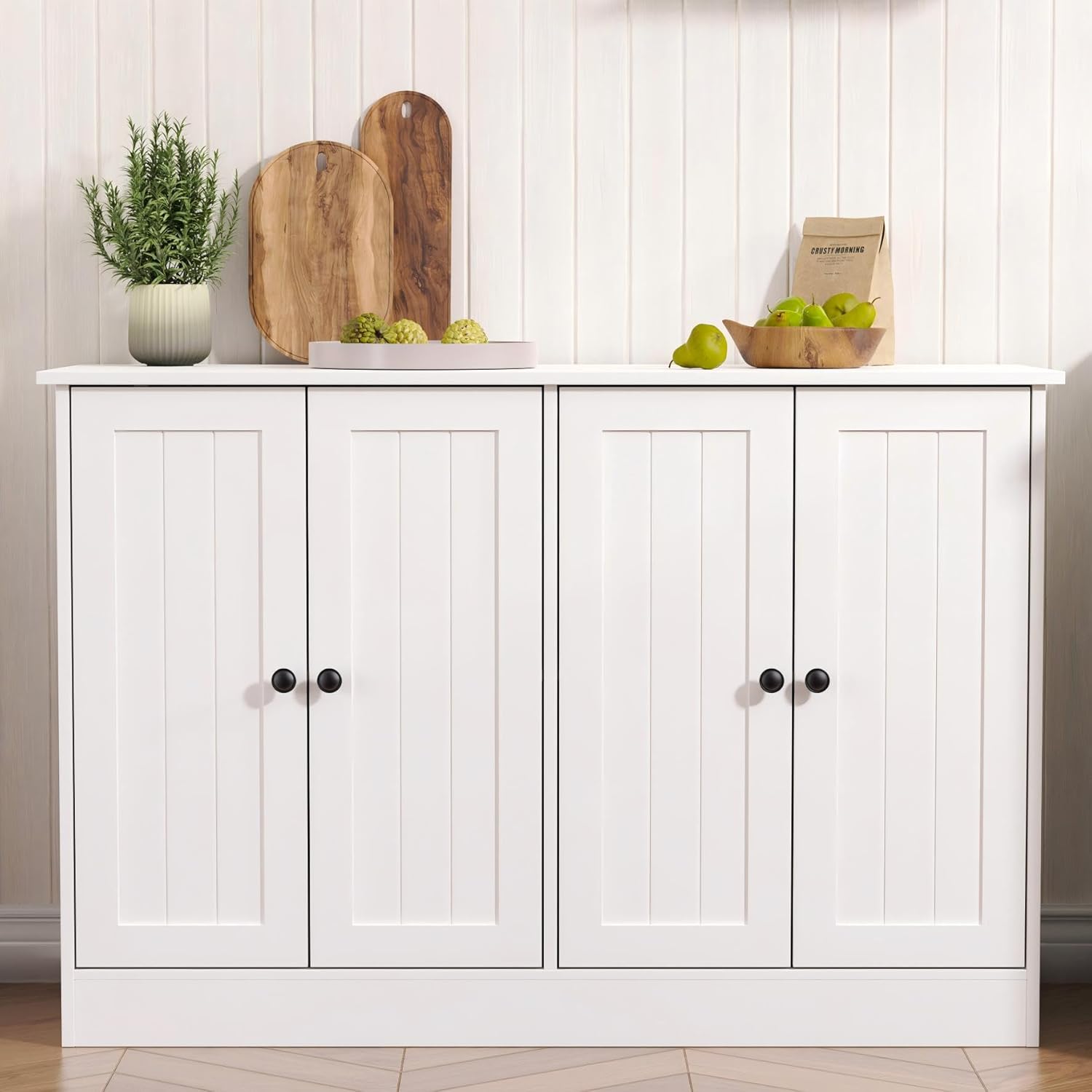 White sideboard buffet cabinet with four doors, featuring a modern farmhouse design, styled with plants and decorative items on top.