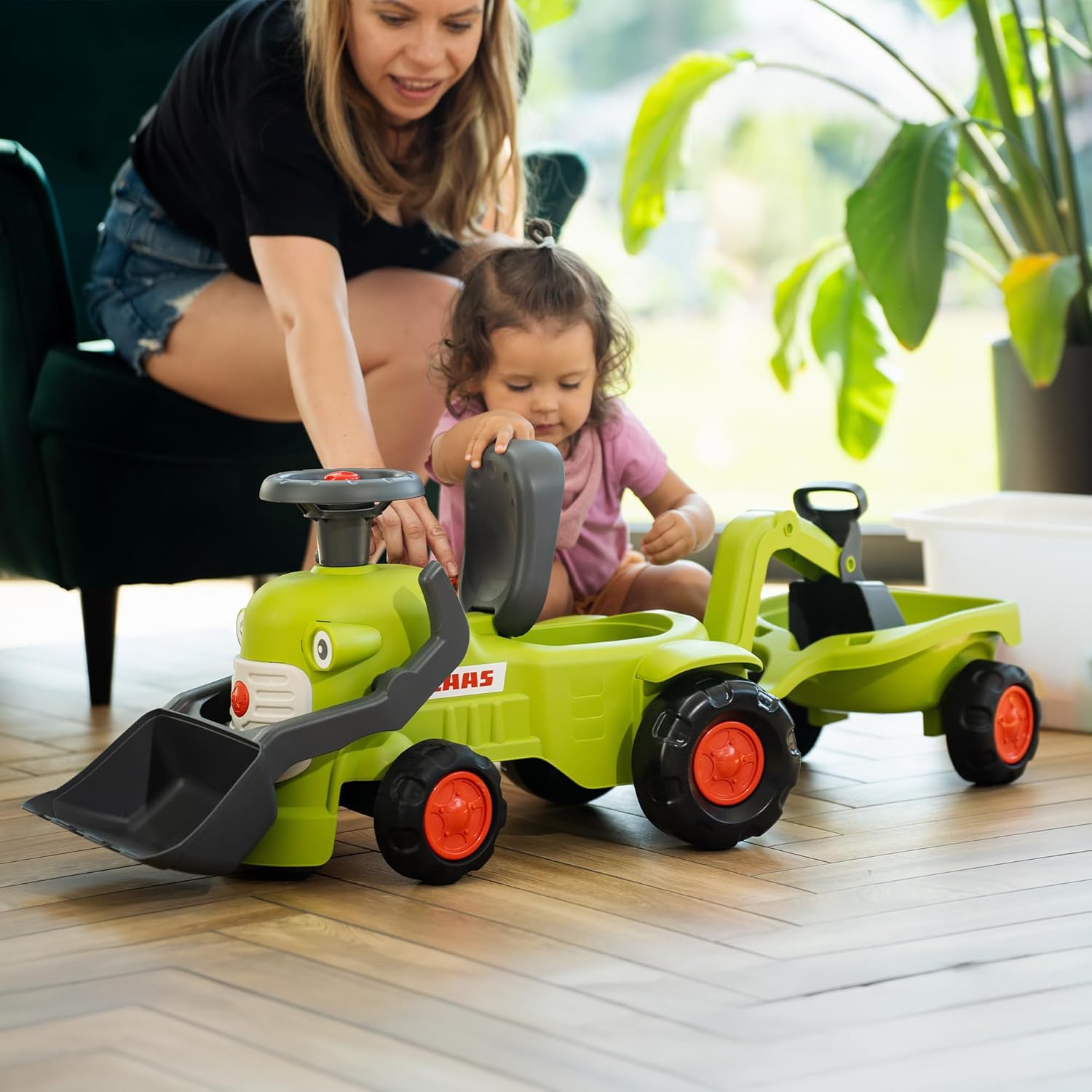 A child and an adult interacting with the Falk Claas Backhoe Loader. The adult is helping the child open the seat to access the storage compartment.