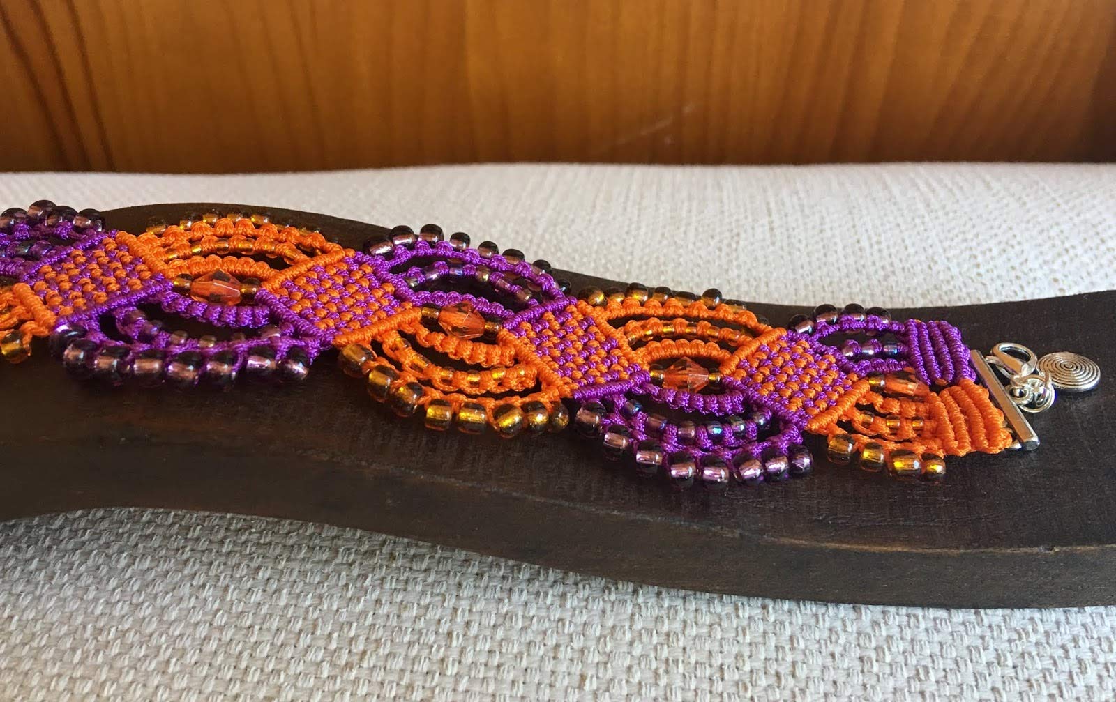 Pulsera macrame morada y naranja hecha a mano con rocallas a juego Cierre y colgante. Mide aproximadamente 17 cm. de largo y 3,5 cm. de ancho