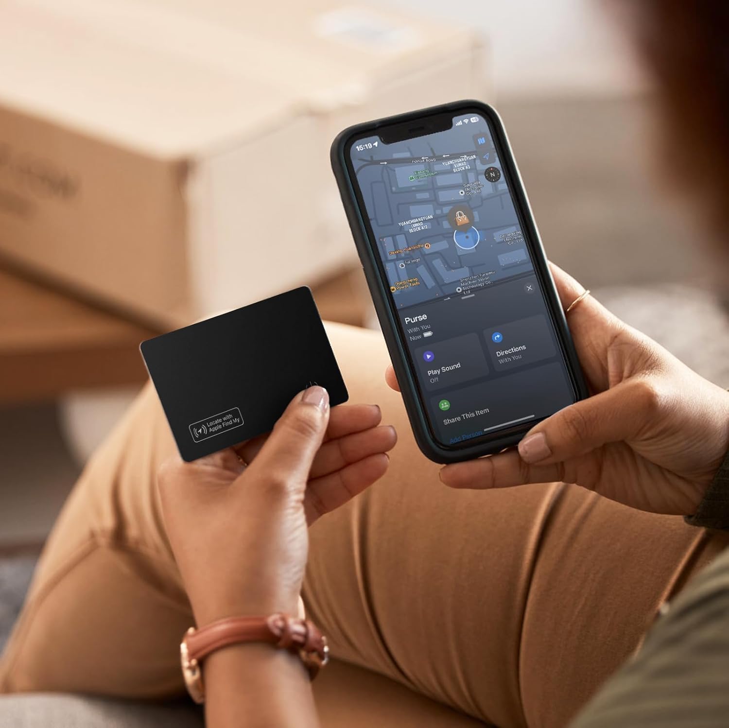 A person holding an iPhone displaying the Apple Find My app with the VODESON Smart Wallet Tracker Card next to it, showing its location on a map.