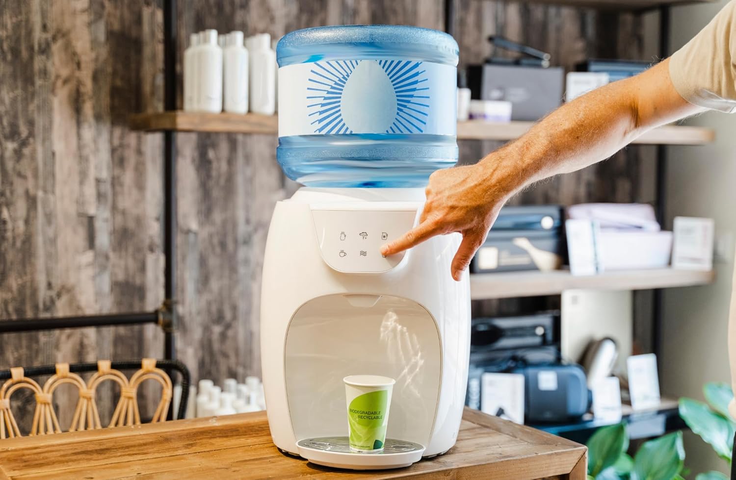 A hand pressing a button on the Primo Touch Compact Water Dispenser to dispense water into a cup