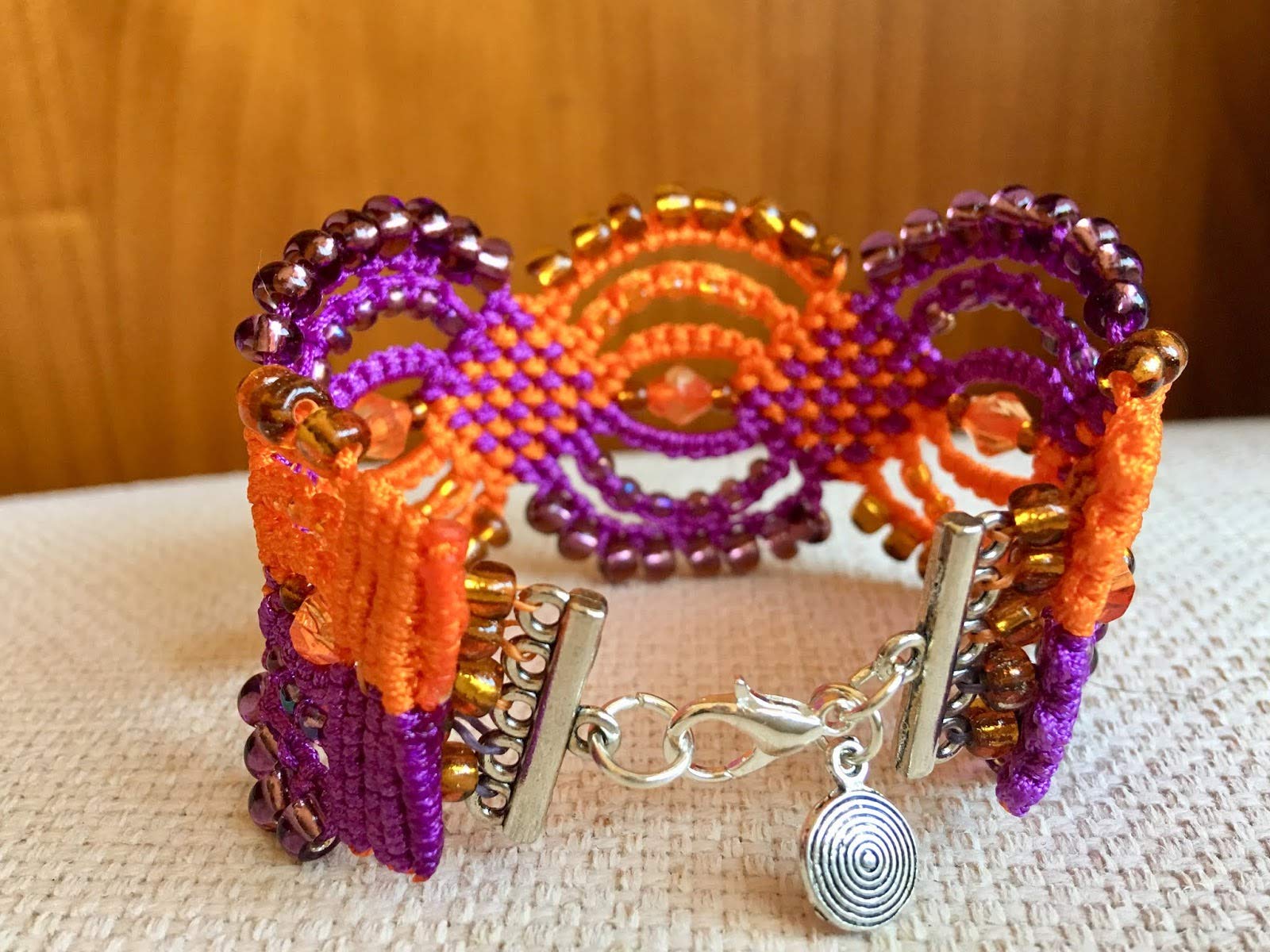 Pulsera macrame morada y naranja hecha a mano con rocallas a juego Cierre y colgante. Mide aproximadamente 17 cm. de largo y 3,5 cm. de ancho