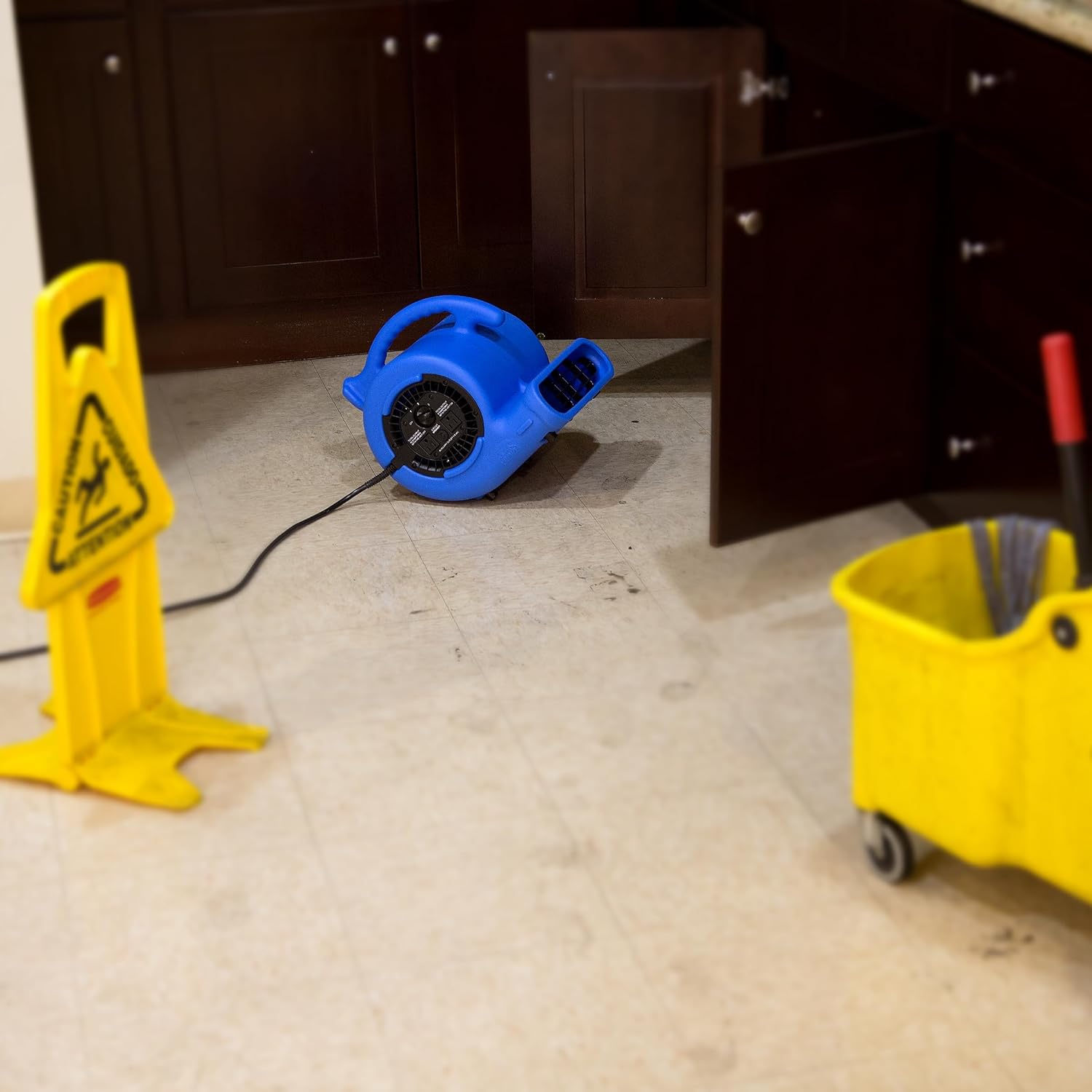 B-Air VP-25 Air Mover in use on a tiled floor next to a wall, with a wet floor sign and mop bucket, illustrating its use for water damage restoration.