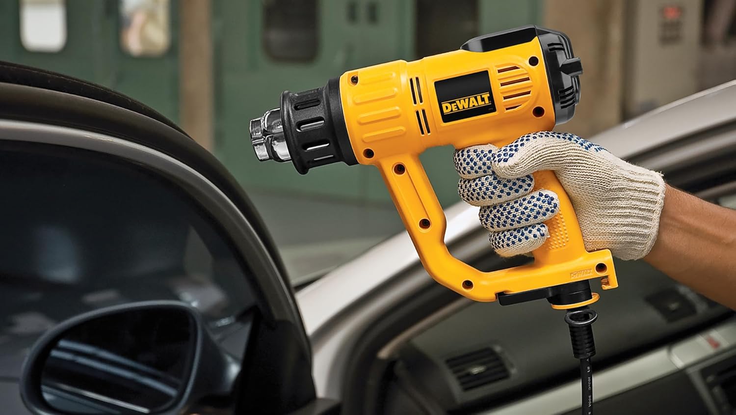 A gloved hand holding the DEWALT heat gun, showing its ergonomic design and ready-to-use state.