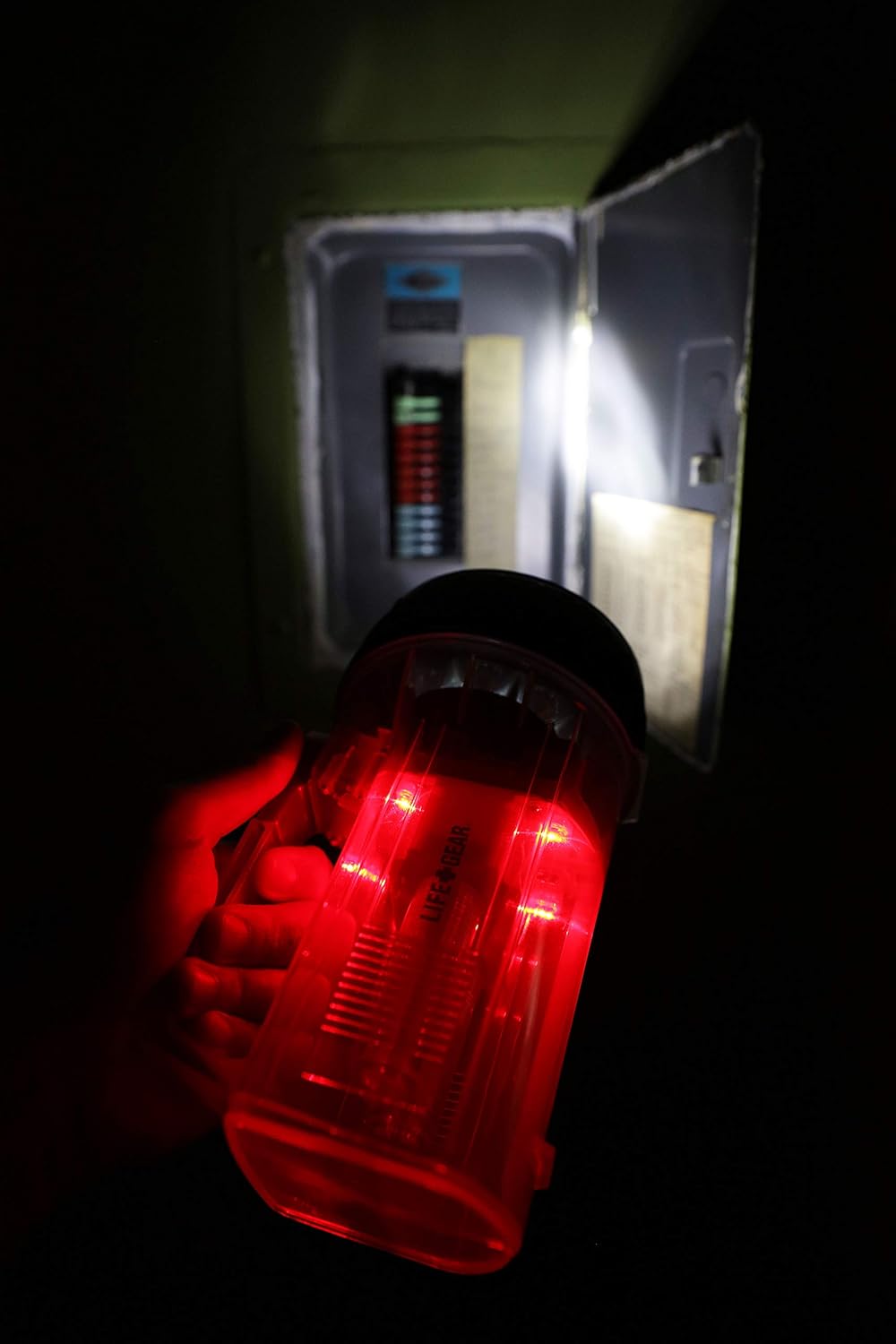 Person holding the Life Gear flashlight in a dark room, illuminating an electrical panel with its red glow and spotlight.