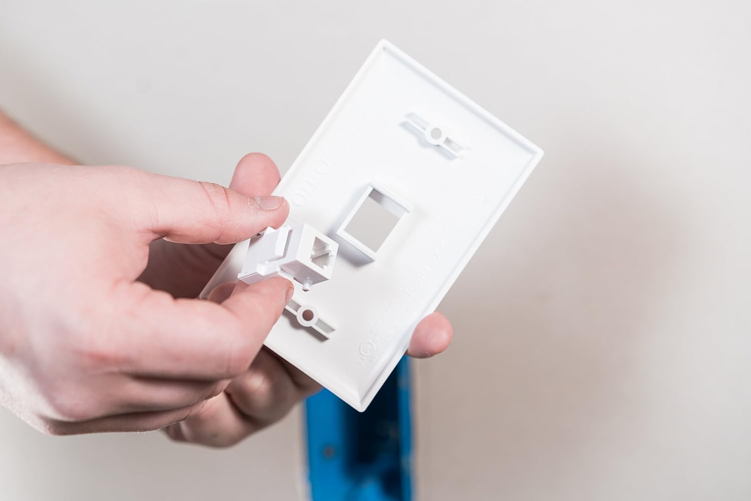 Hand inserting the Legrand On-Q RJ25 Telephone Keystone Jack into a white wall plate.