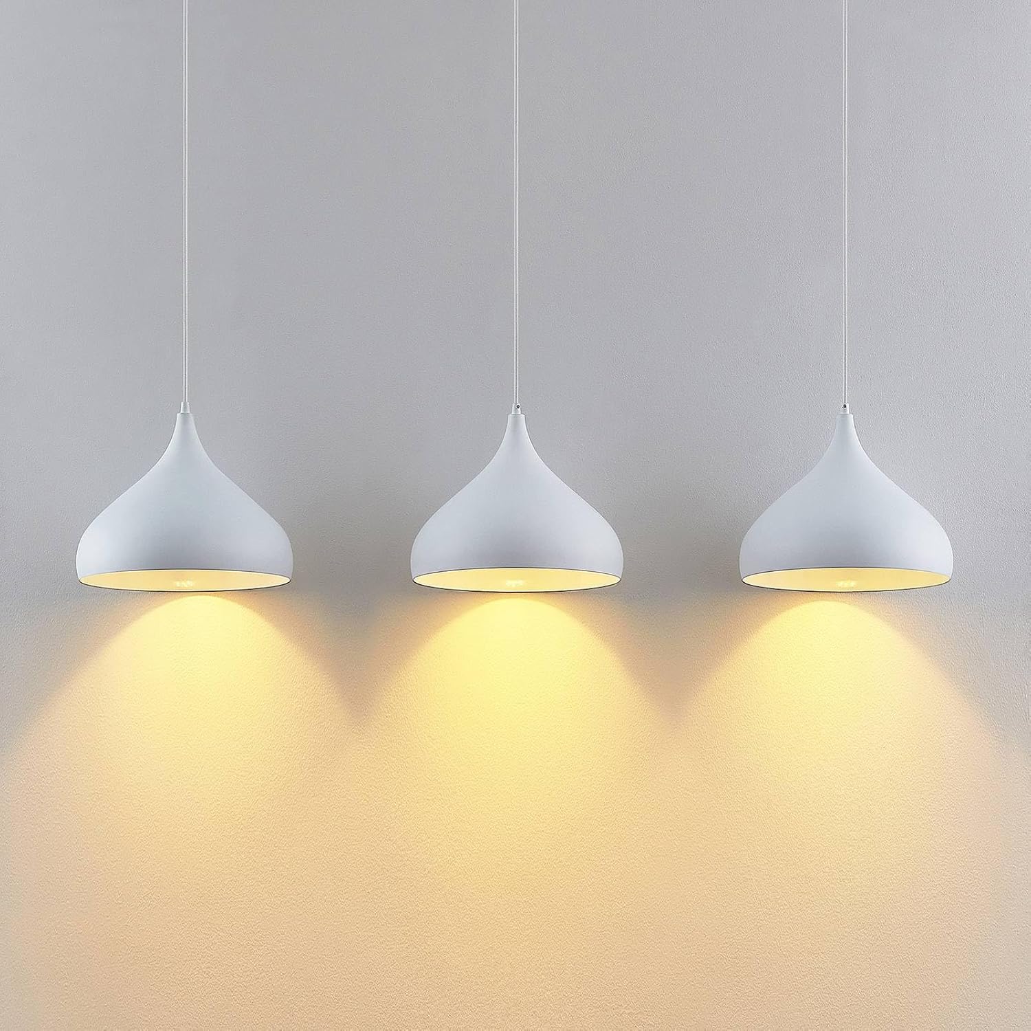 Close-up of the three Lindby Elamira pendant lamp shades casting warm light downwards onto a wall, highlighting the light distribution.