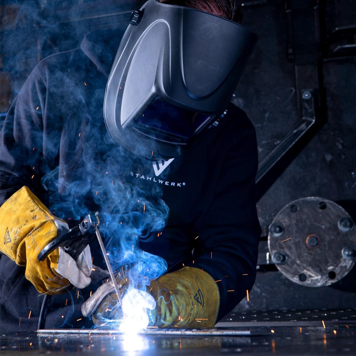 A welder wearing the STAHLWERK ST-900 XTC automatic welding helmet during active welding, with sparks visible.
