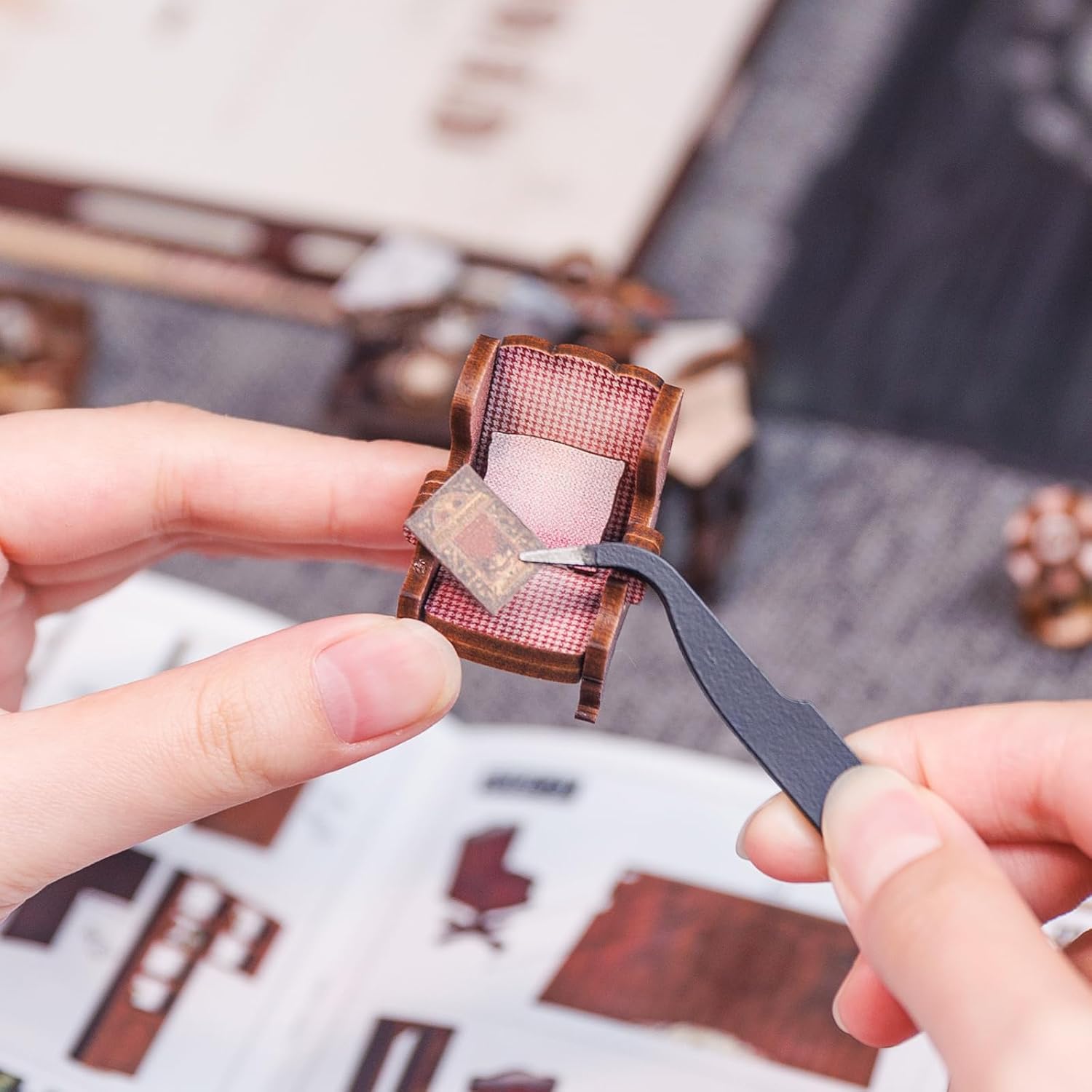 Hands using tweezers to place a small miniature book onto a chair