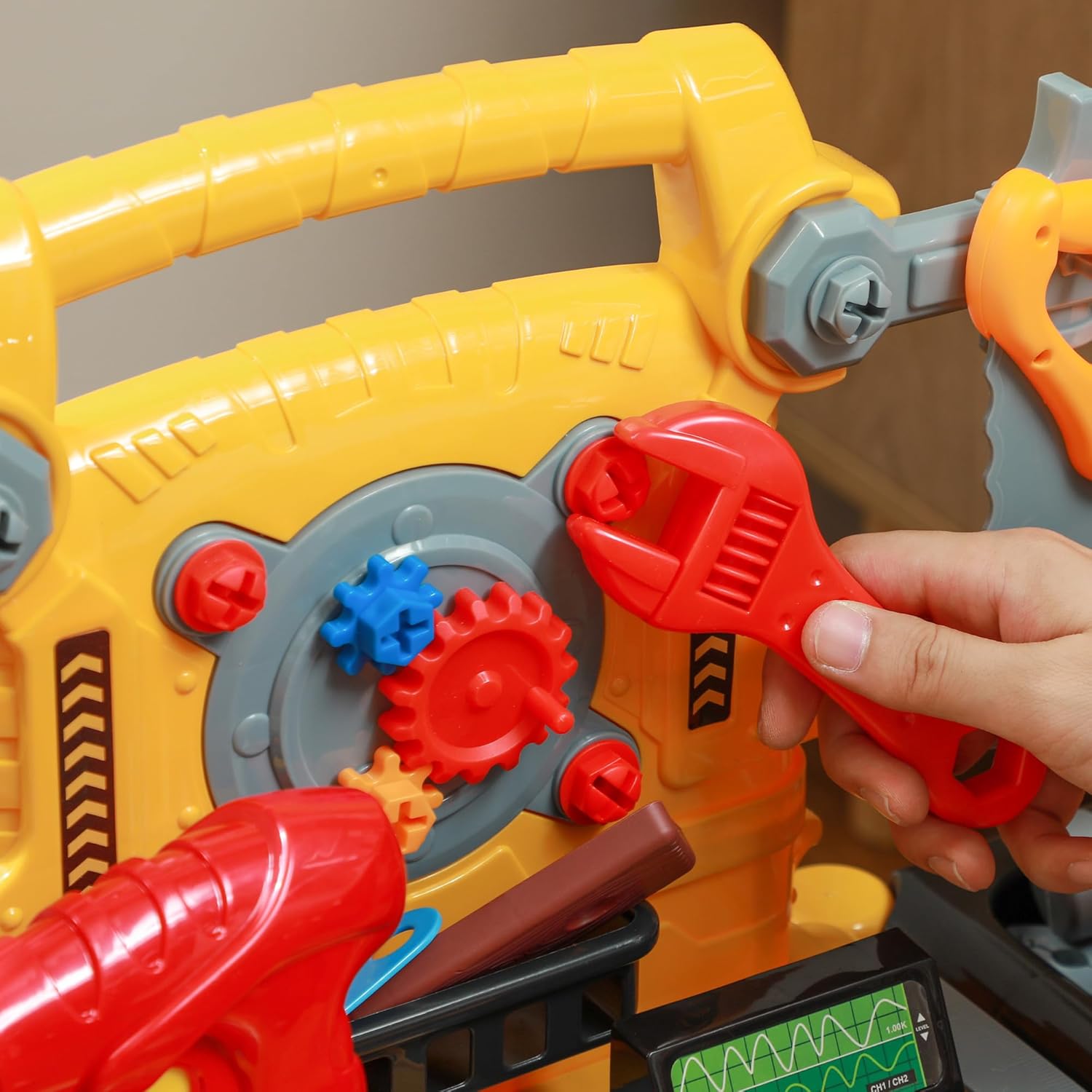 La mano de un niño usando una llave de juguete para girar un engranaje en el banco de herramientas para niños AIYAPLAY