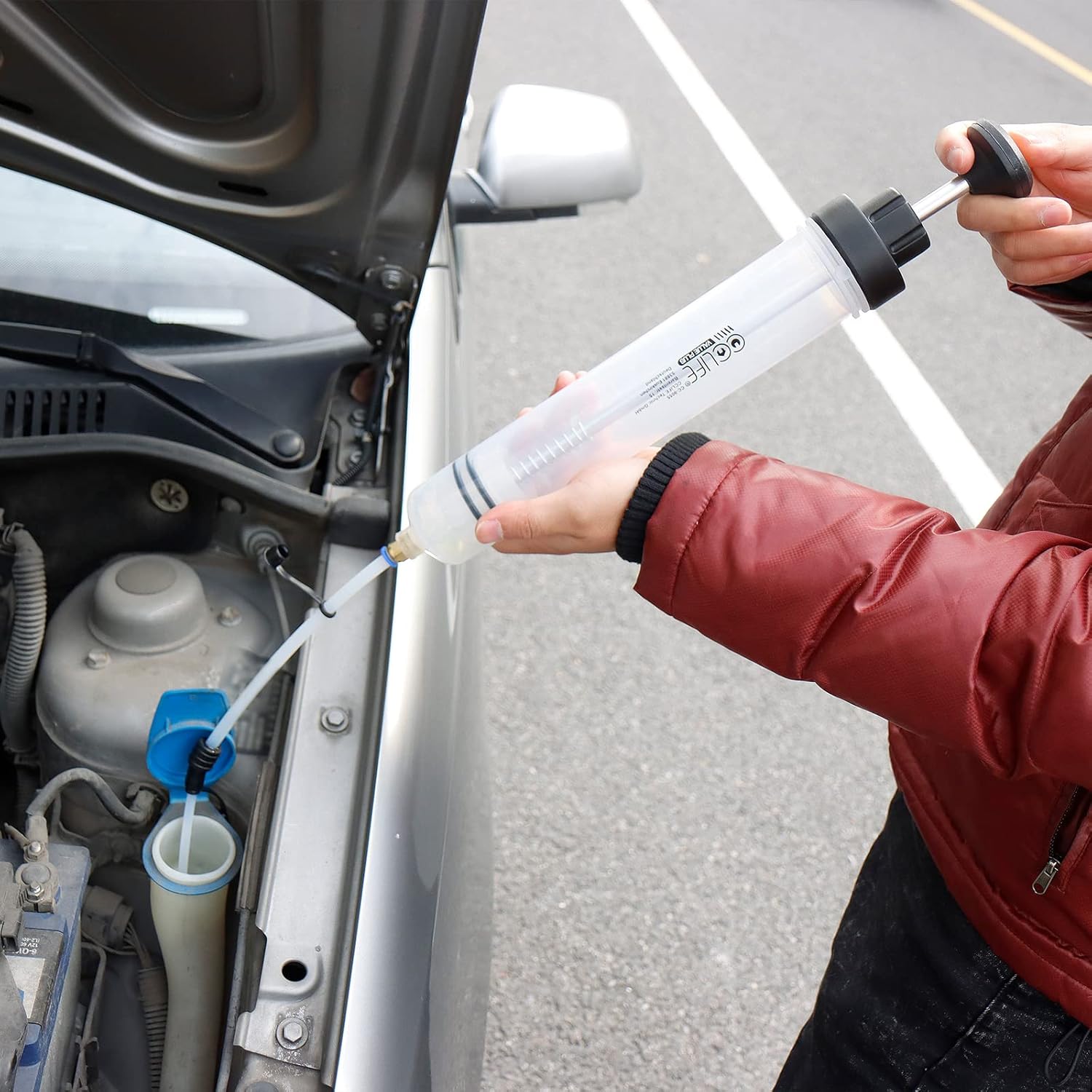 A person using the CCLIFE fluid extractor to remove fluid from a car's engine bay, likely brake fluid from a reservoir.
