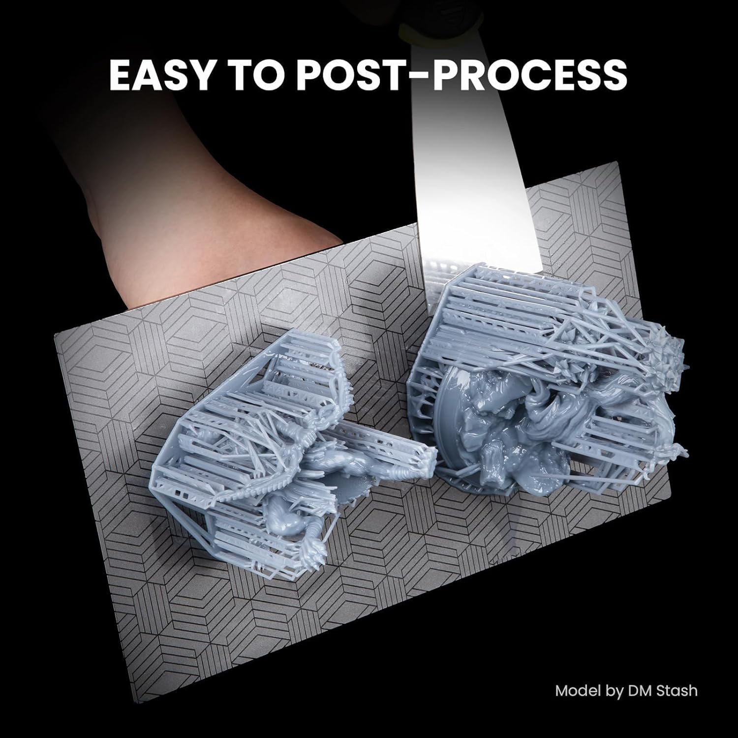 A hand using a metal spatula to easily remove two 3D printed models from a build plate, demonstrating the ease of post-processing.