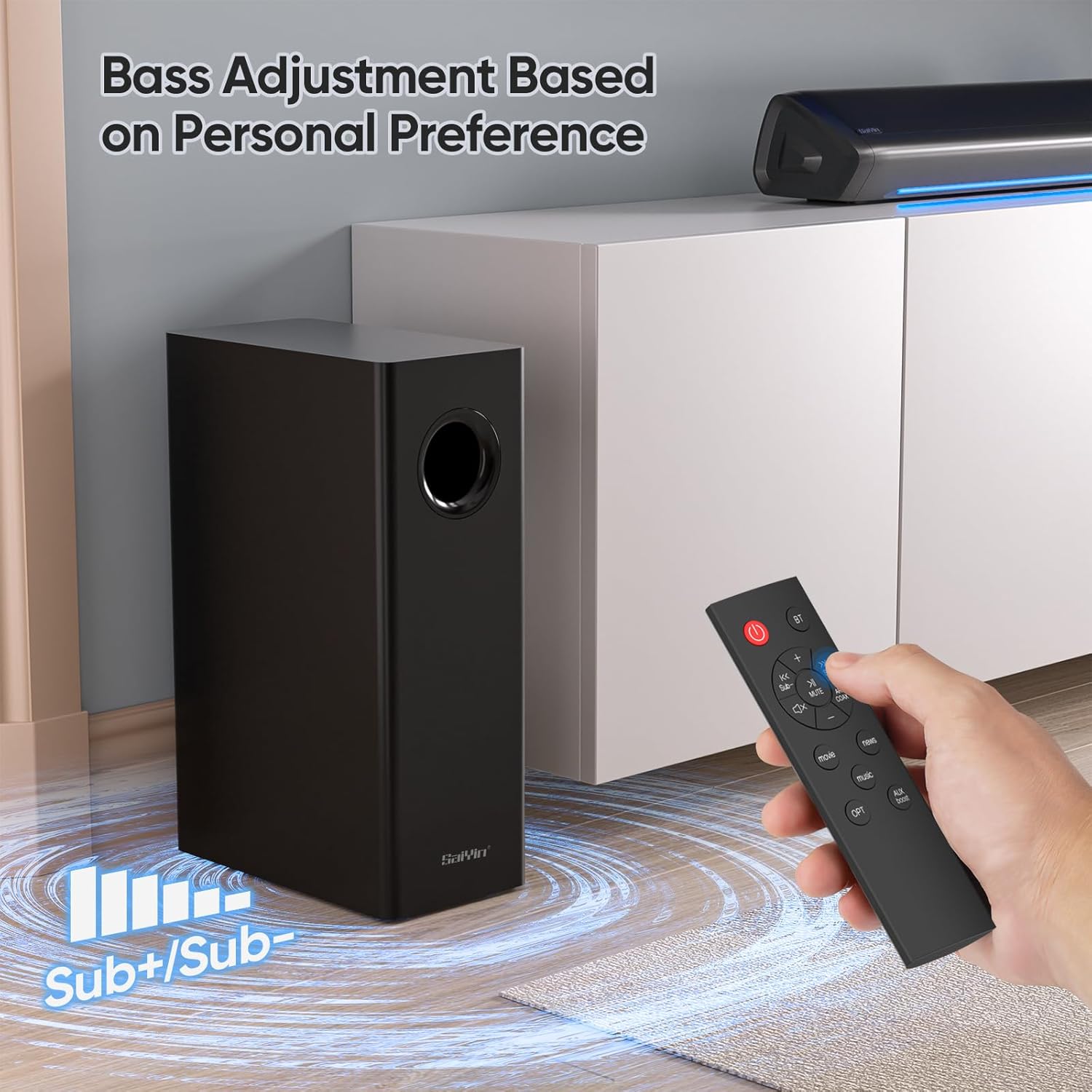 A hand holding the remote control for the Saiyin Soundbar, with the subwoofer in the background.